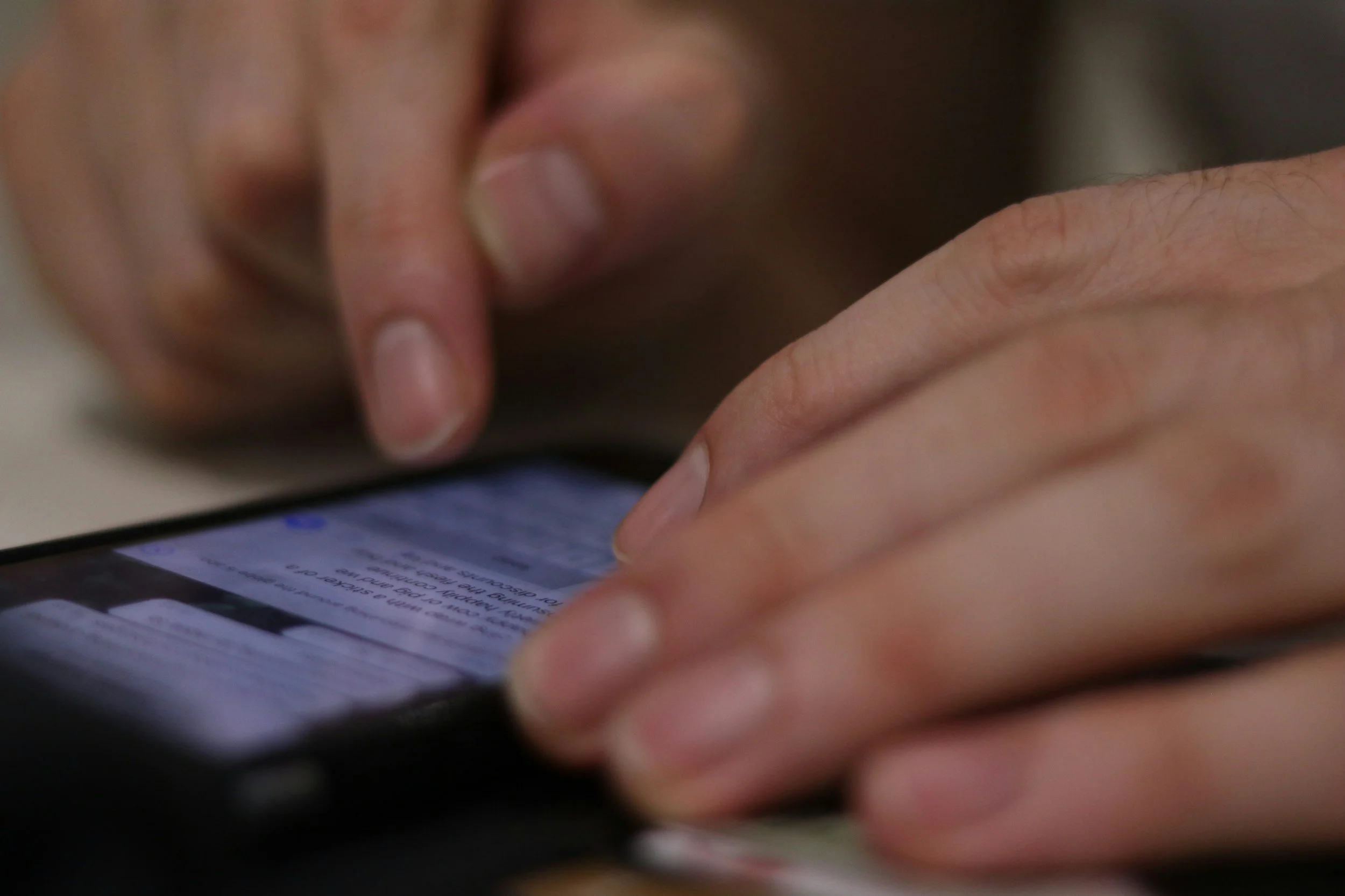 Close-up of a person's hand with fingers touching a smartphone screen, which displays text, possibly reading or typing.