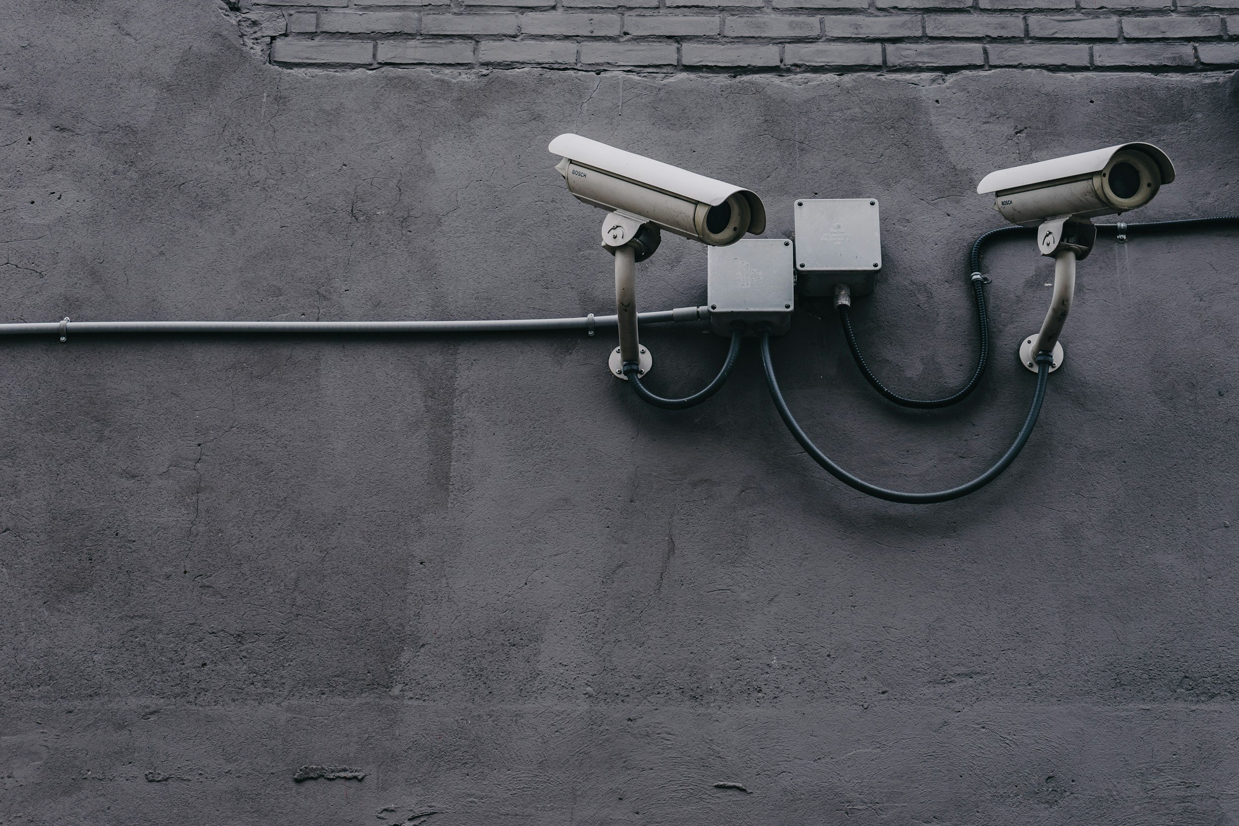 Two security cameras mounted on a gray concrete wall.