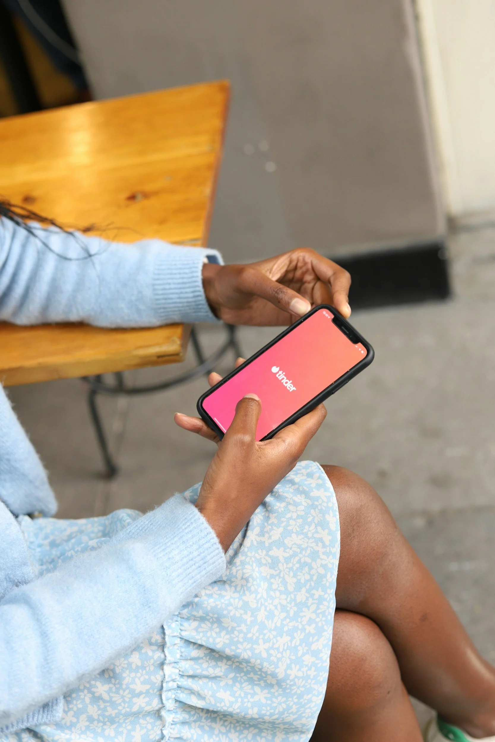 Person sitting on a wooden chair using a smartphone with the Tinder app open.
