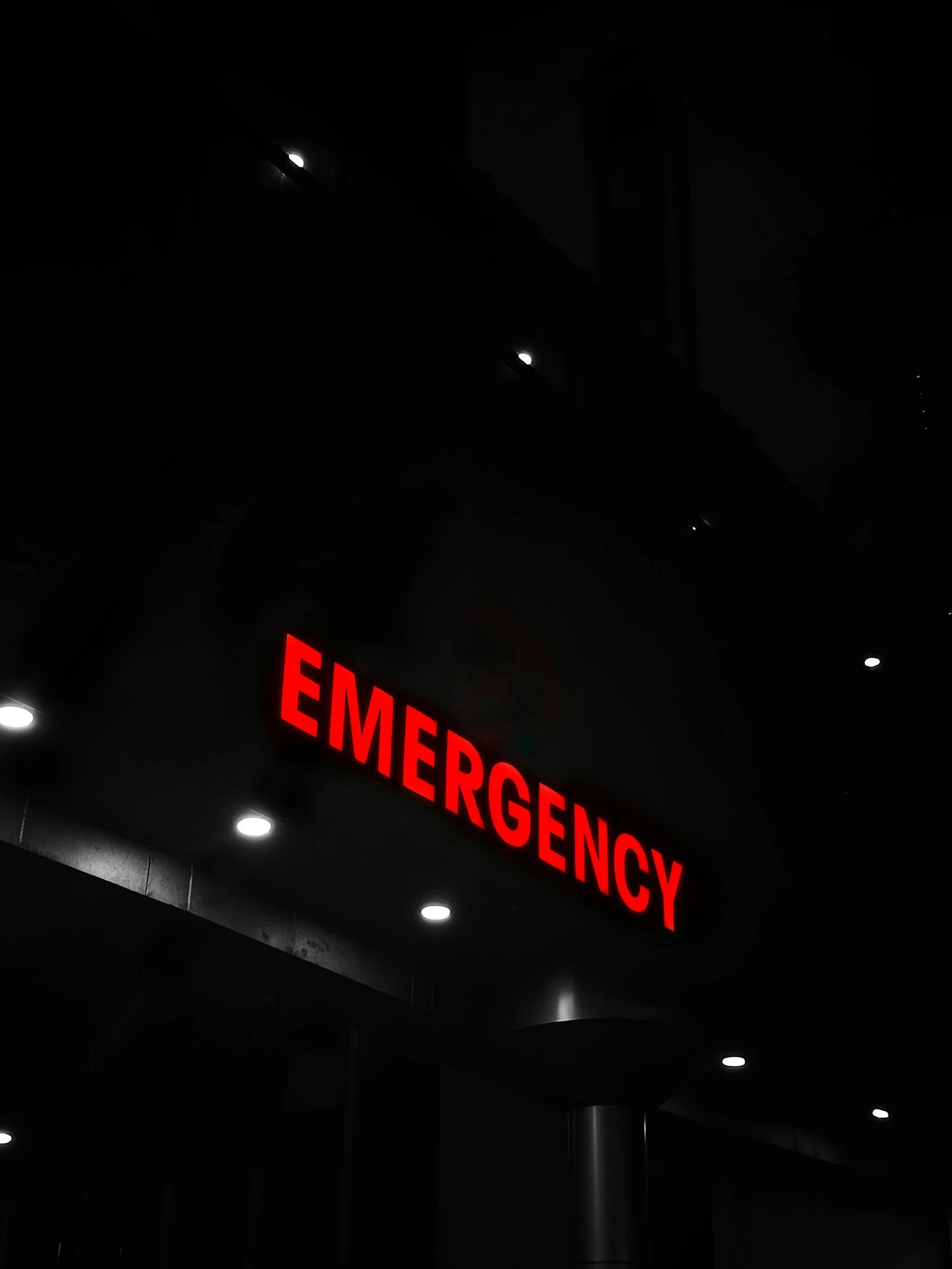 Red illuminated emergency sign at night with only part visible, spelling out "EMERGENCY."