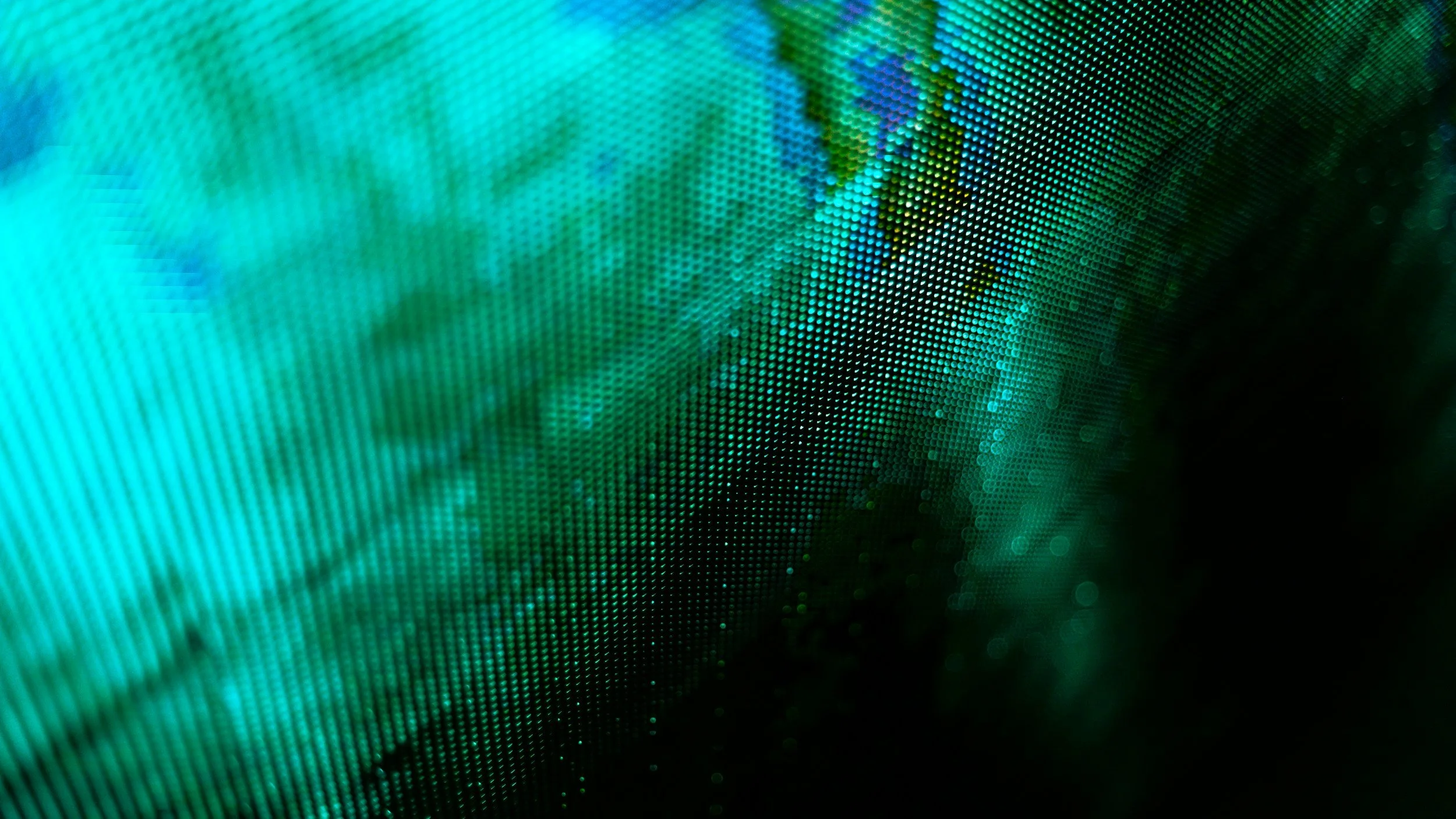 Close-up of a computer screen with a pattern of colorful, pixel-like dots in shades of blue, green, and yellow, creating an abstract digital background.