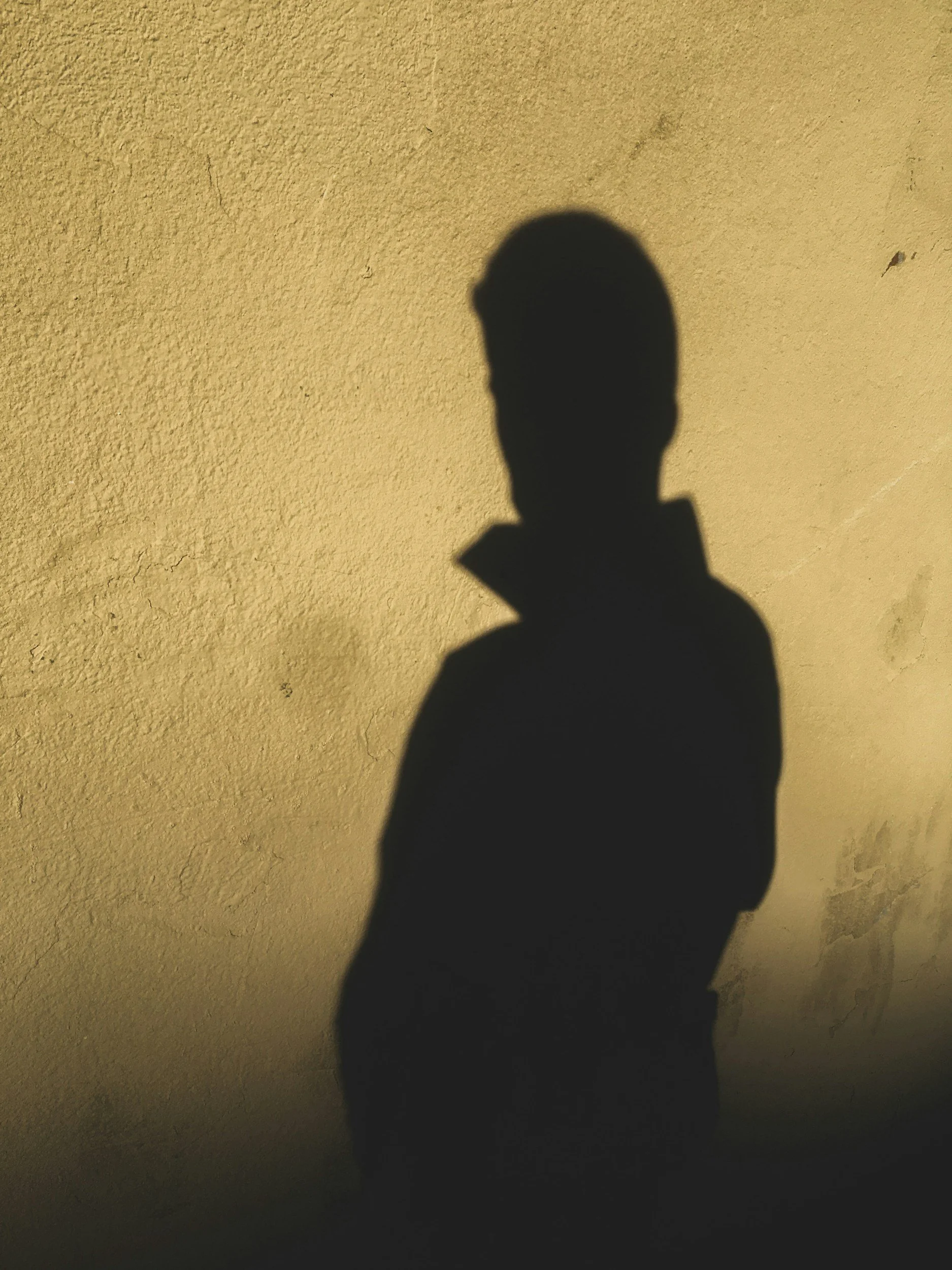 Shadow of a person’s head and shoulders cast on a plain, beige wall.