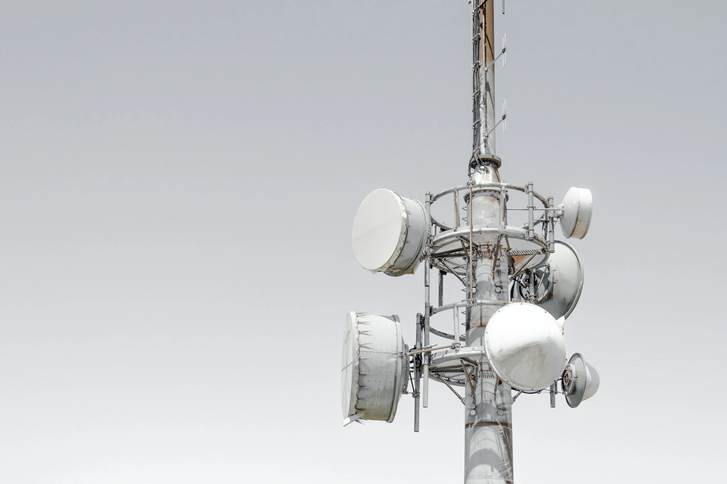 A tall communications tower with multiple white satellite dishes mounted on it, set against a cloudy sky.