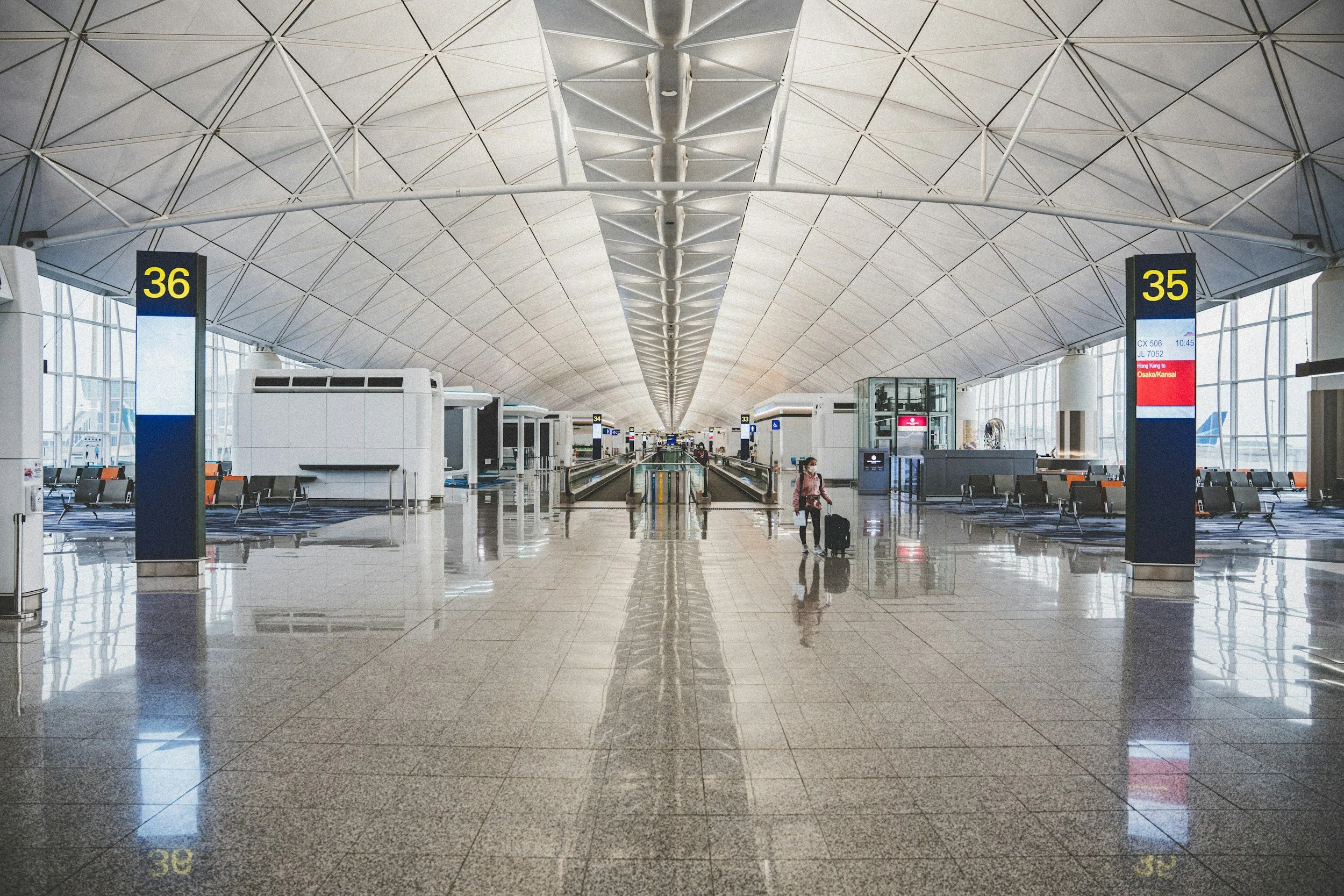 Interior of an airport with gates 35 and 36, modern ceiling structure, large windows, and a woman pulling a suitcase.