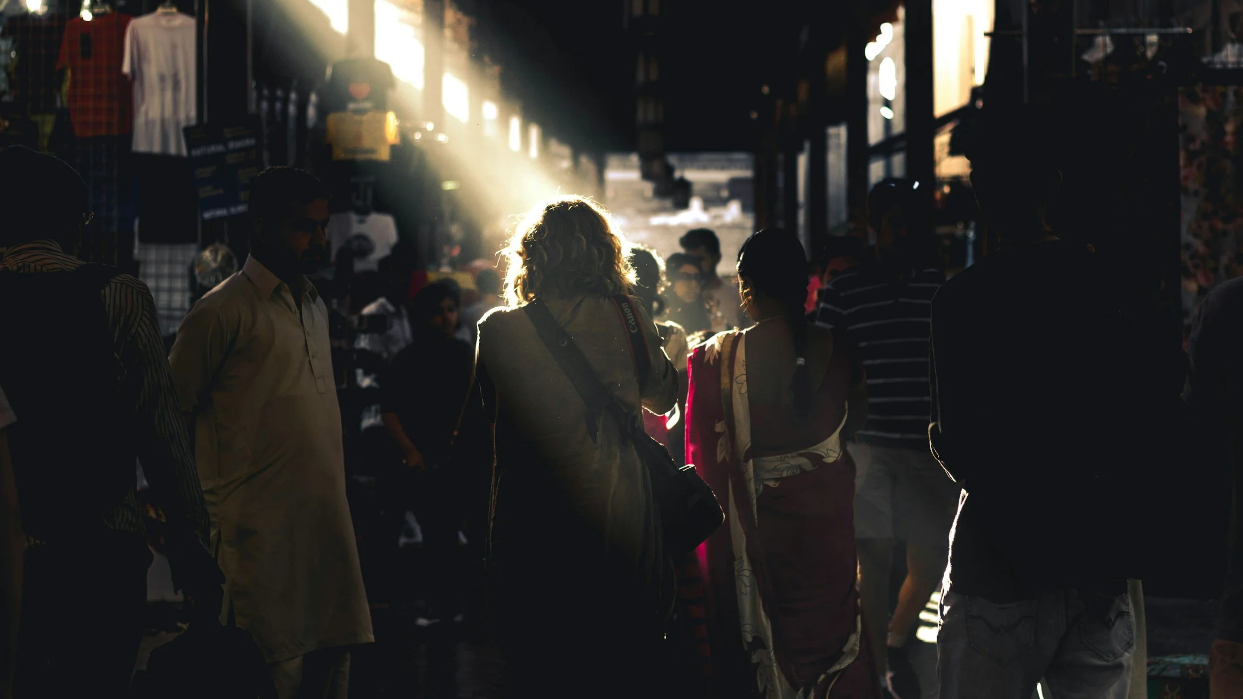 A busy street scene with people walking in silhouette against bright sunlight streaming in from behind.