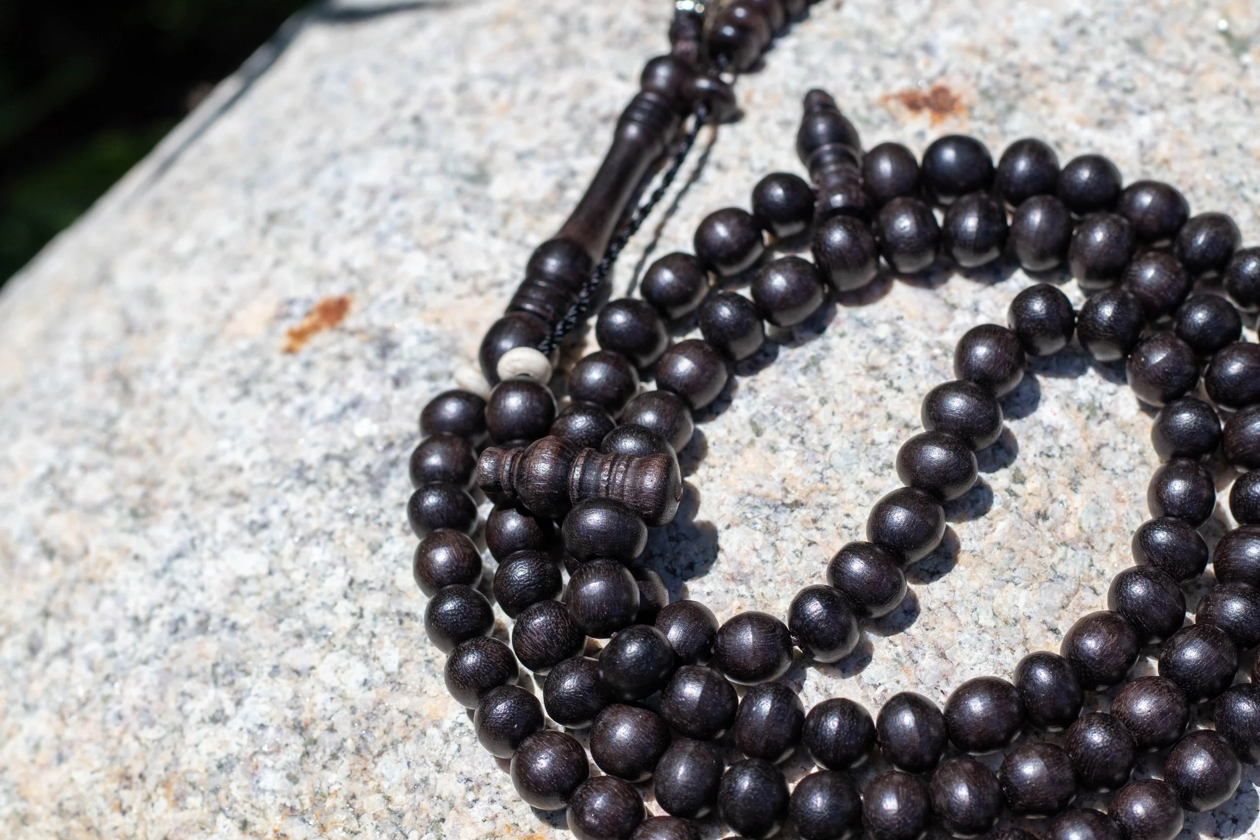 Close-up of a string of dark wooden prayer beads on a light gray stone surface.