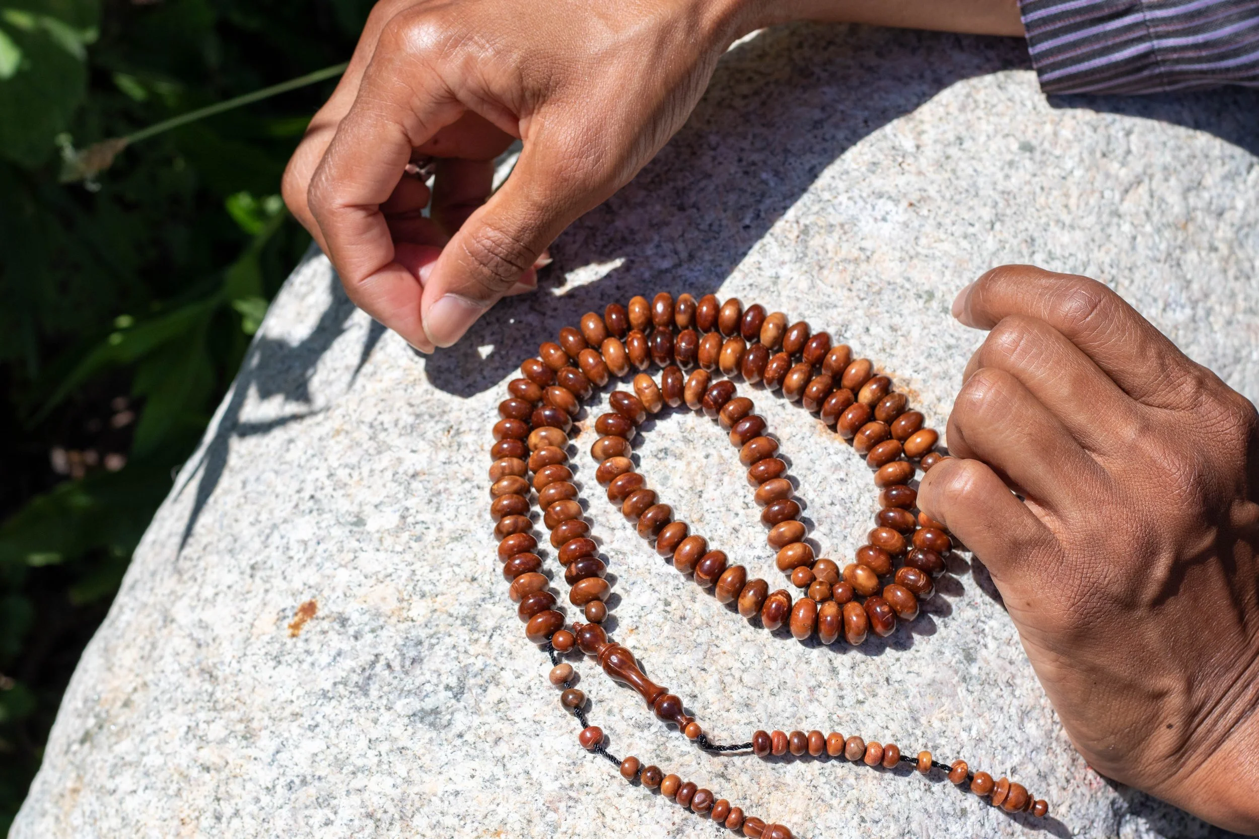 Hands arranging a wooden prayer beads on a stone surface outdoors.