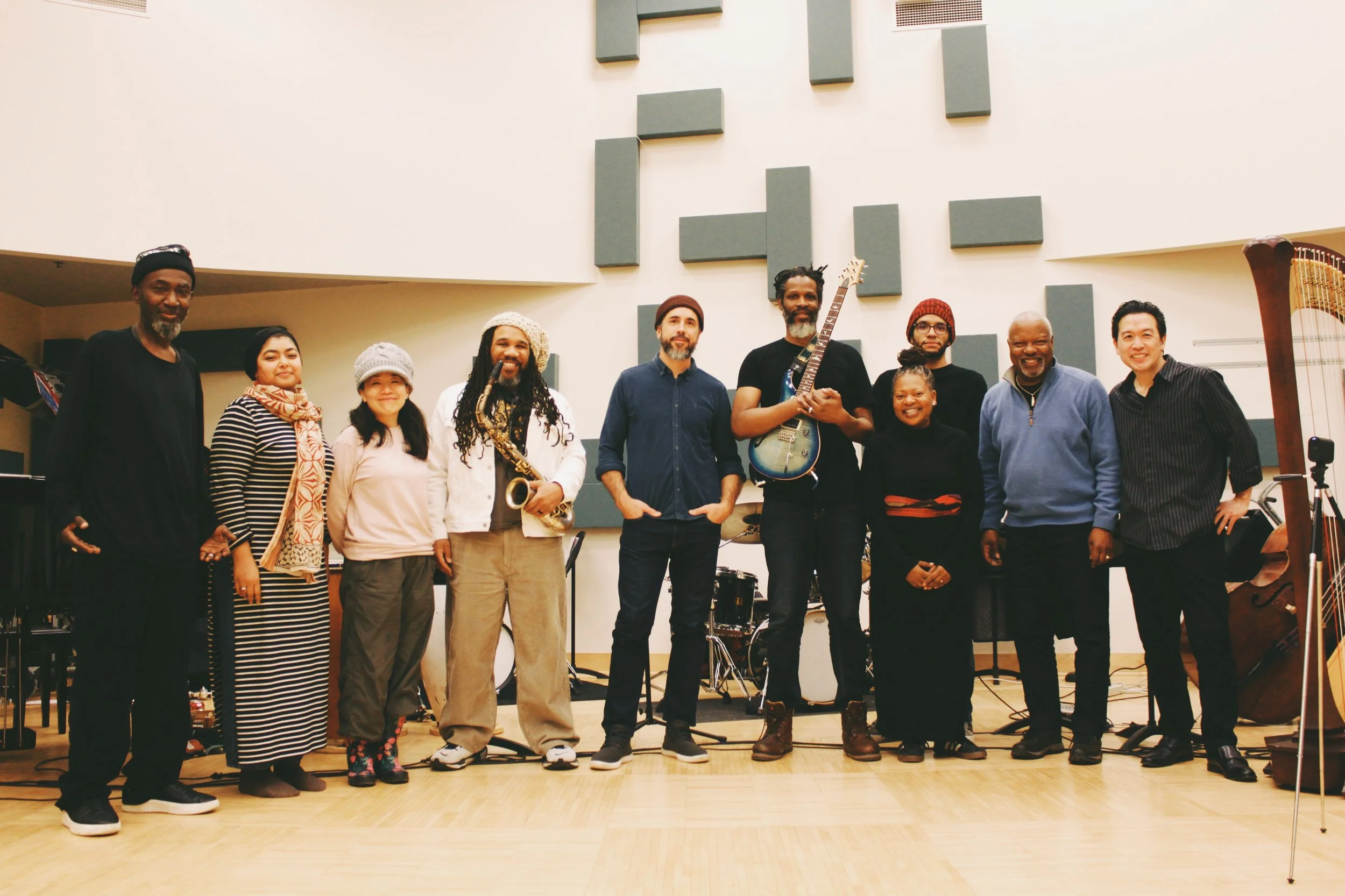 Group of eleven diverse musicians standing in a music studio with instruments.