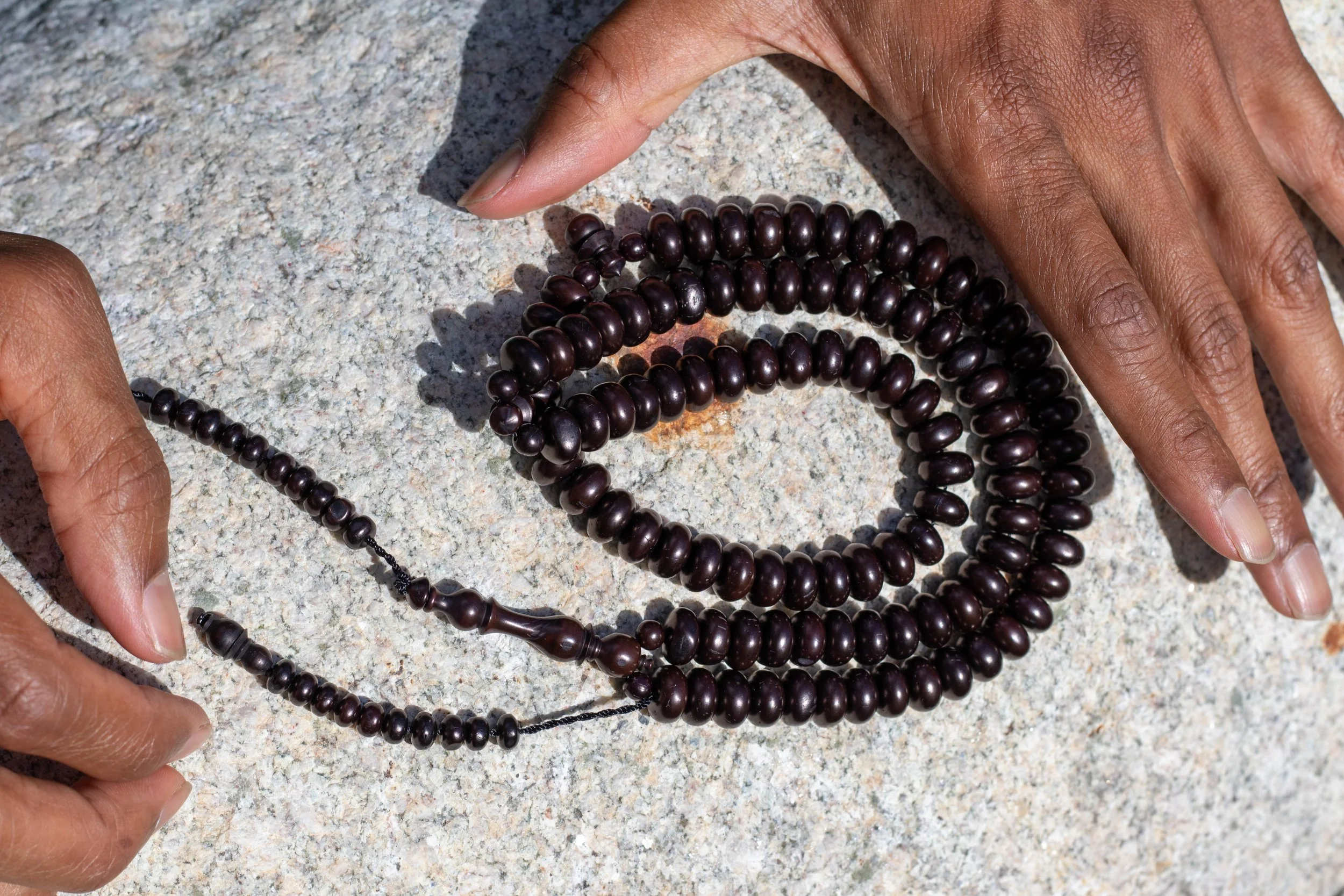 Dark wooden prayer beads laid on a light rock surface, held between hands.