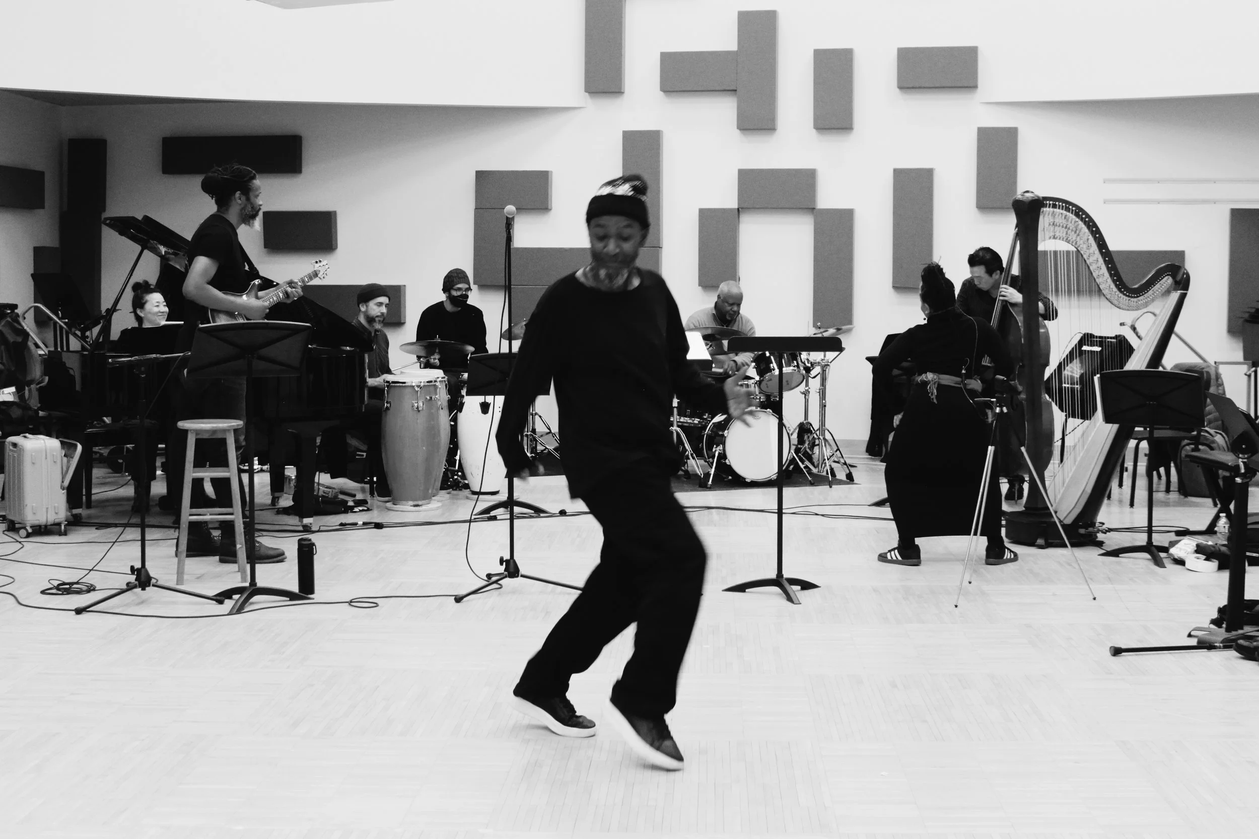 A man dancing in front of a jazz band in a studio with acoustic panels on the wall.