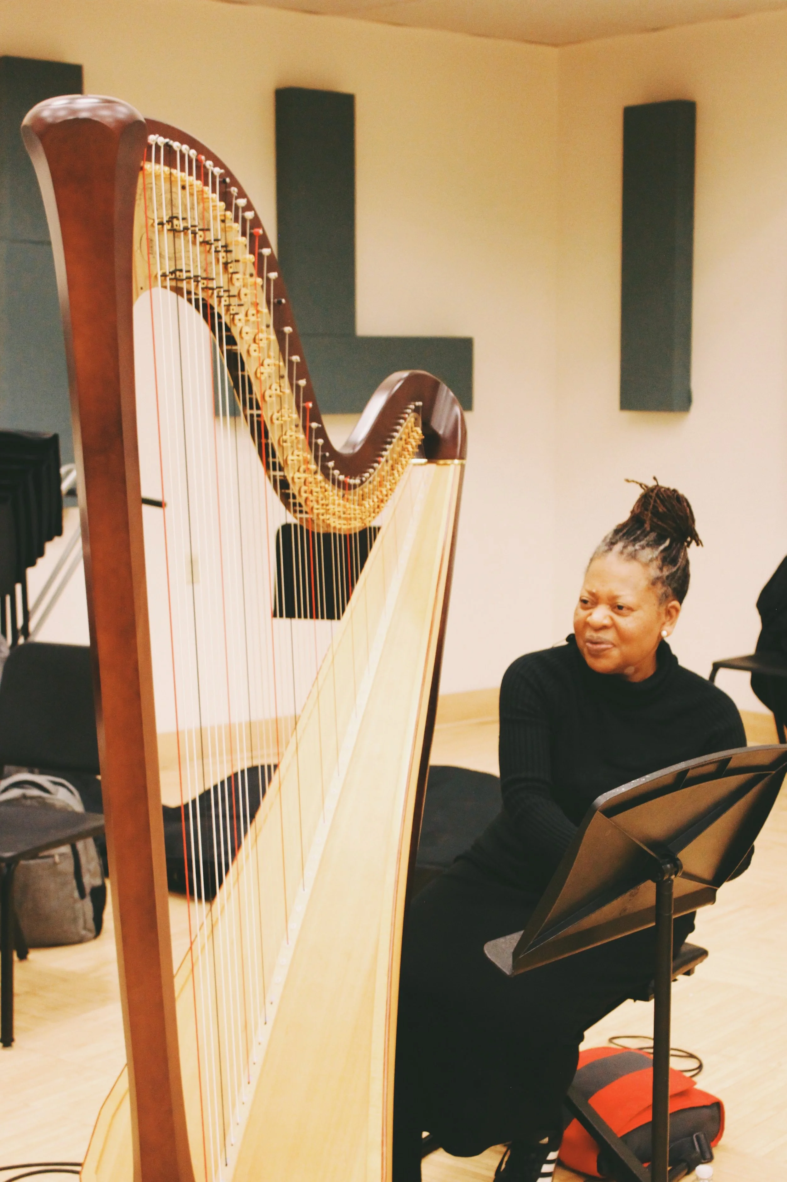 A woman sitting in front of a harpsichord with a sheet music stand in a music studio.