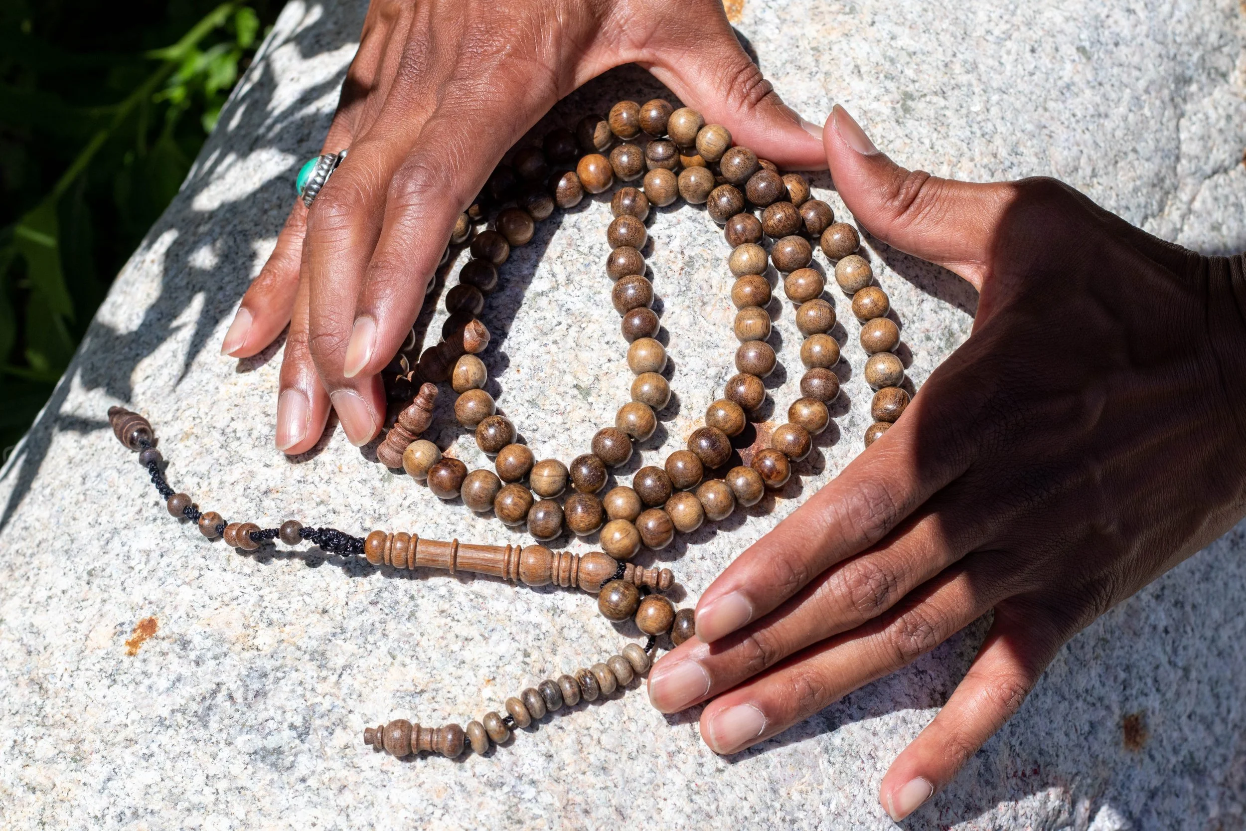 Person displaying multiple strands of wooden prayer beads on a light-colored stone surface outdoors.