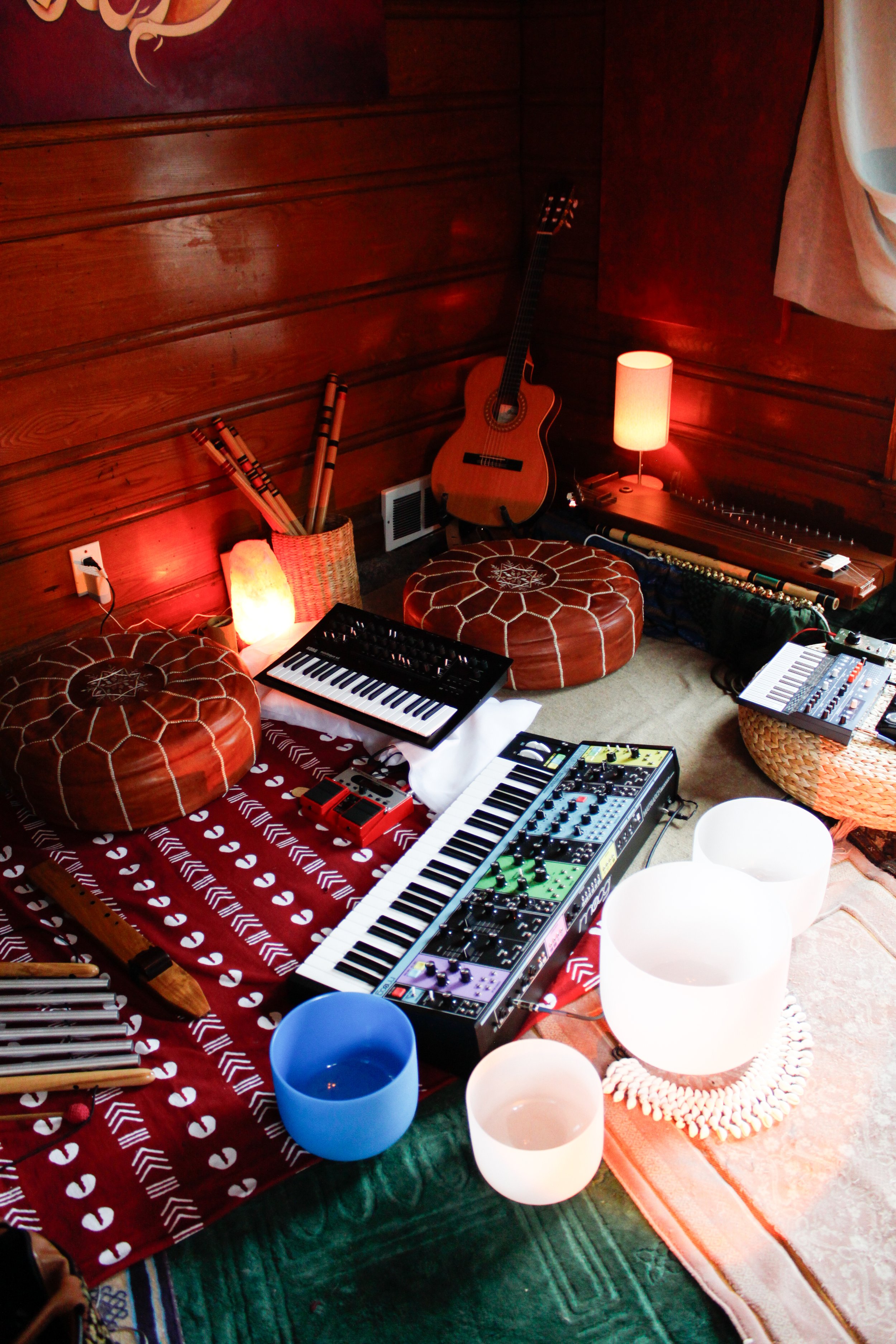 A cozy music corner with musical instruments and equipment, including a keyboard, a synthesizer, an acoustic guitar, a kalimba, and various percussion instruments, all set against warm wooden walls with soft lighting.
