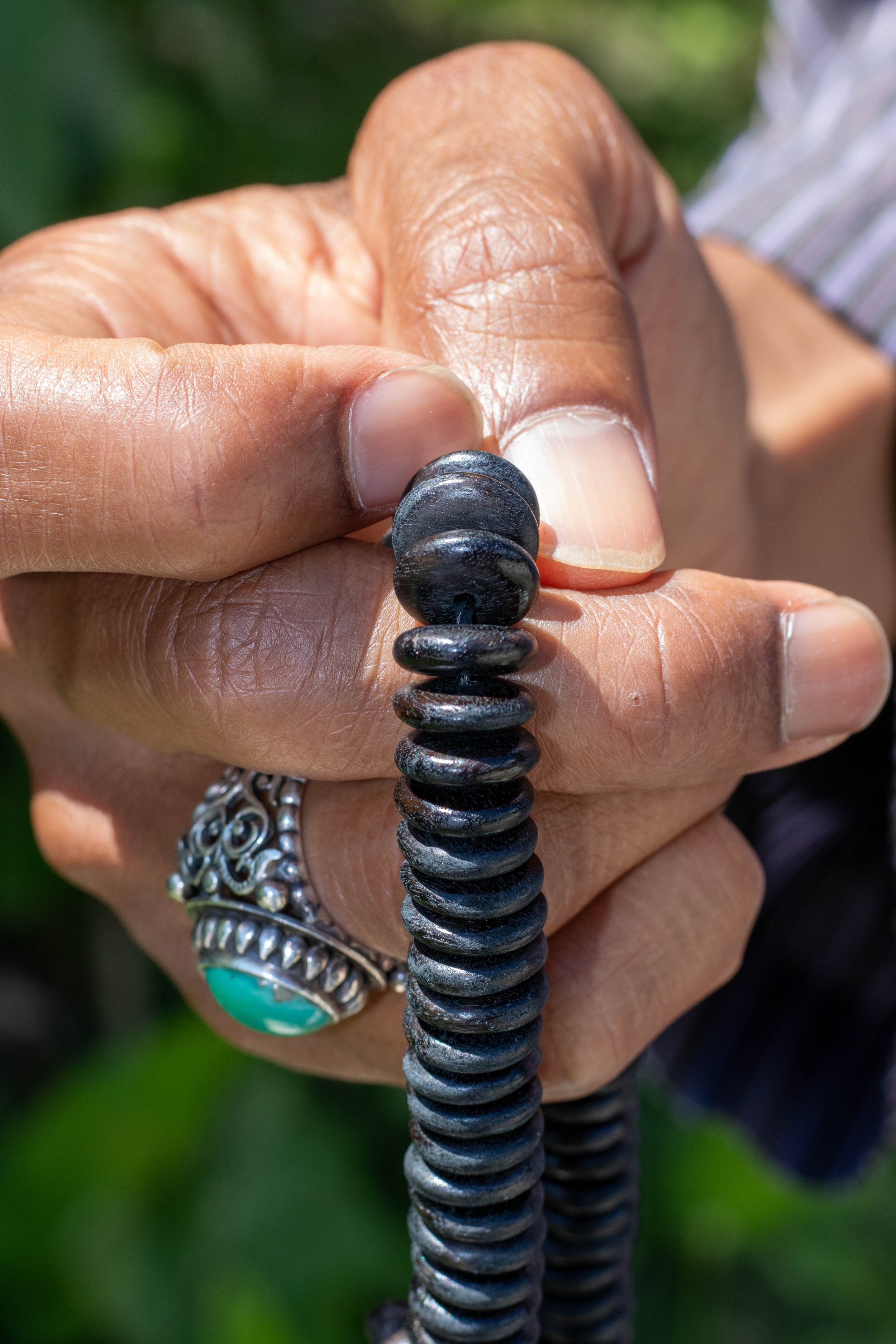 Close-up of a hand holding a black coiled object, possibly a spring or copper wire, with a large silver ring featuring green stone on the person's finger.