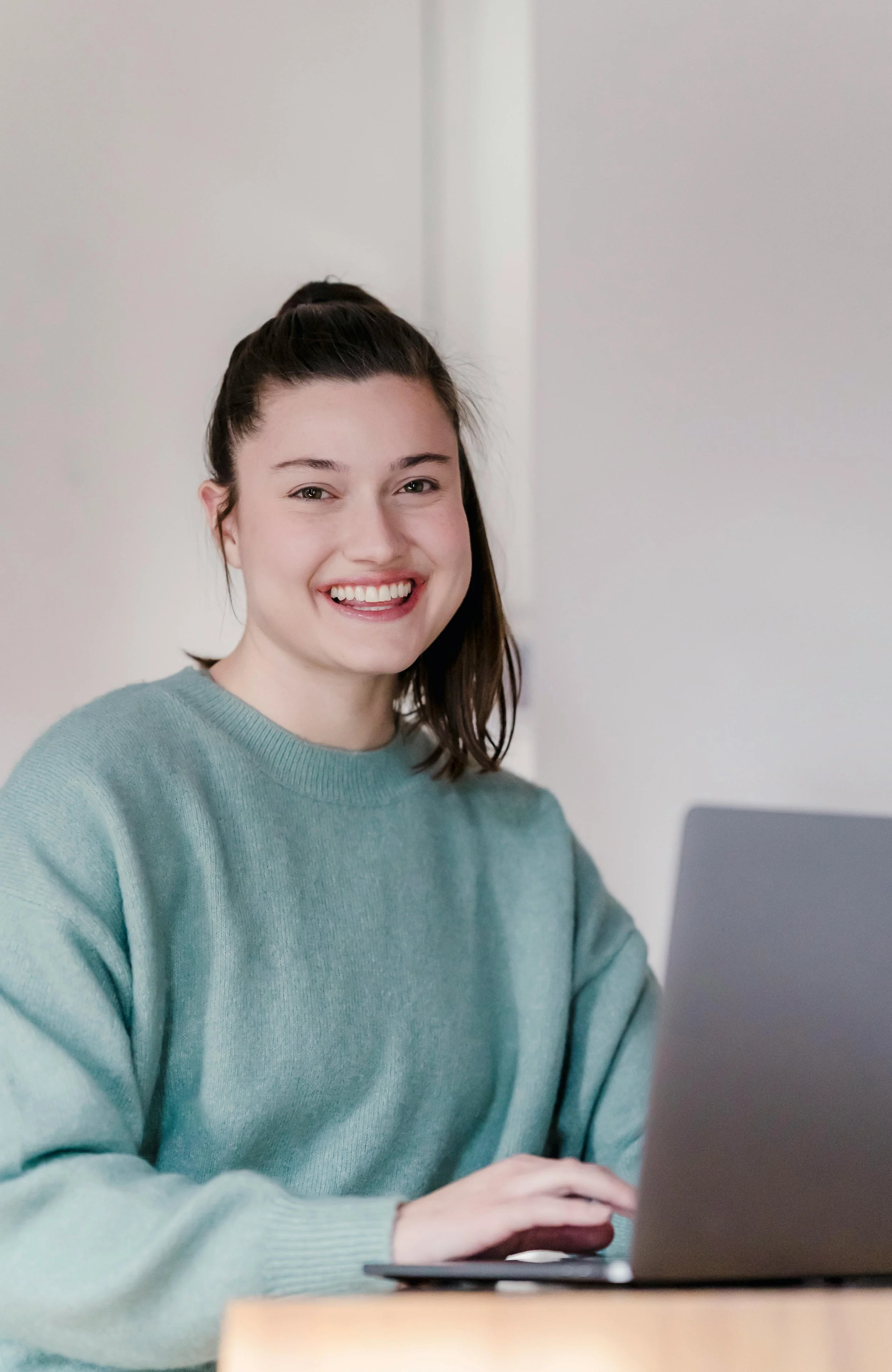 A young woman smiling while working on a laptop at a desk.