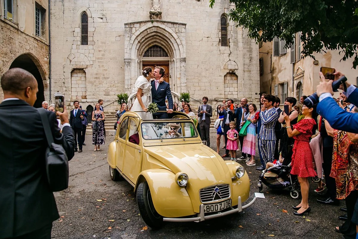 Newlyweds exiting the church with an old classic car while kissing