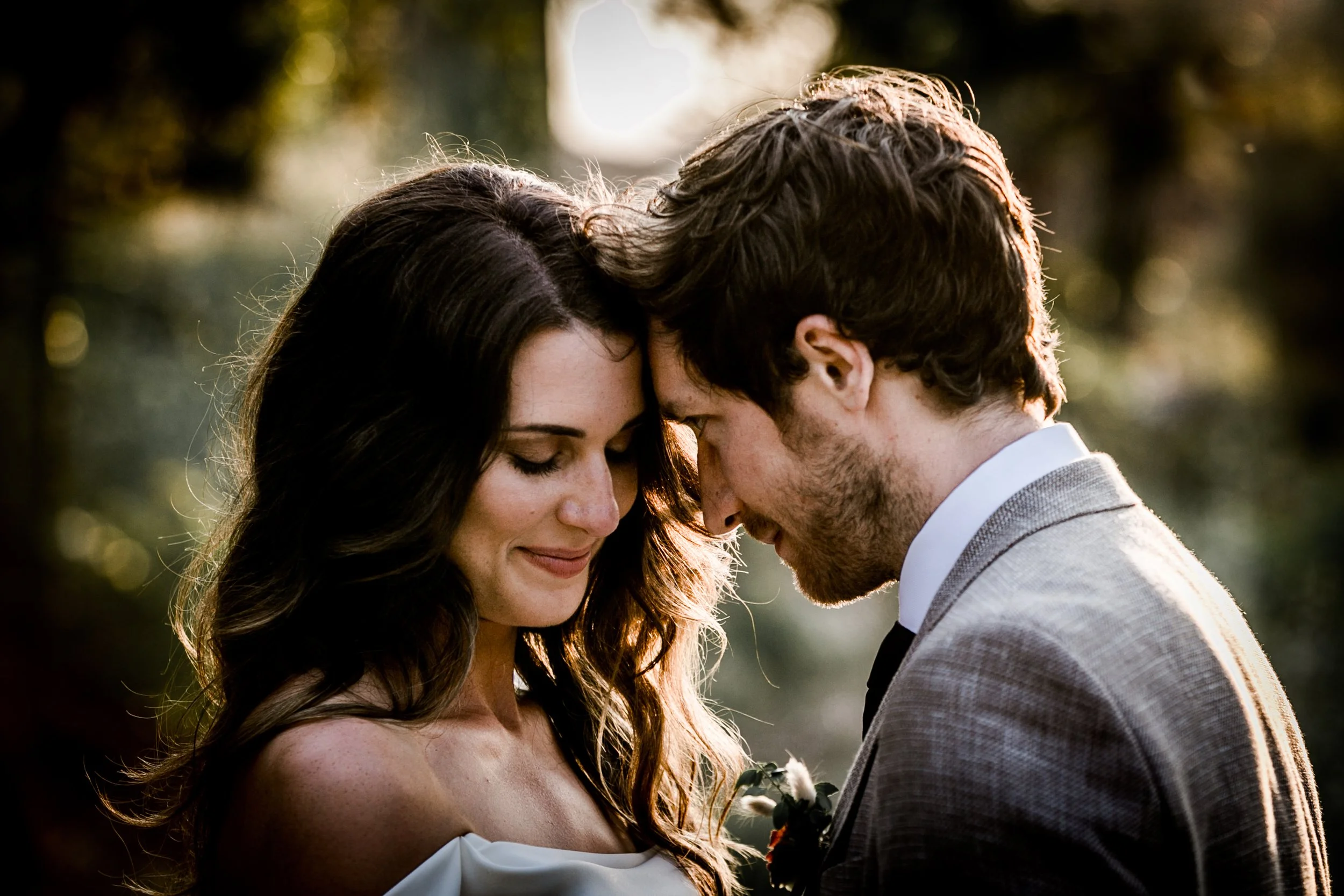 A close-up of a couple with their foreheads touching, smiling gently, in an outdoor setting with warm sunlight and blurred greenery in the background during their photo time at their wedding at casa felix, barcelona