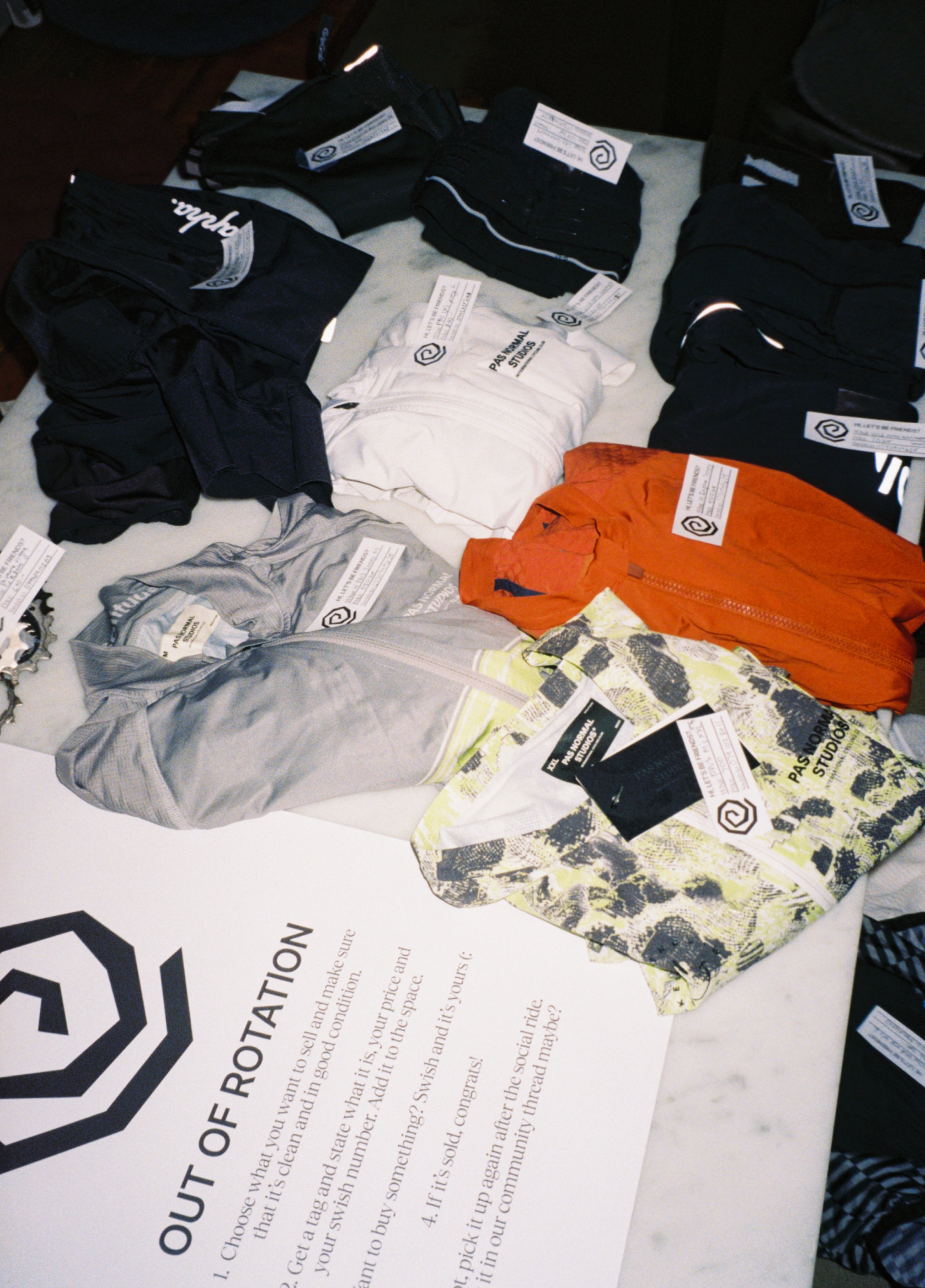 Several folded pairs of athletic shorts and a few shirts are spread out on a table, each with tags attached. There is a paper with the logo and text about OUT OF ROTATION on the table as well.