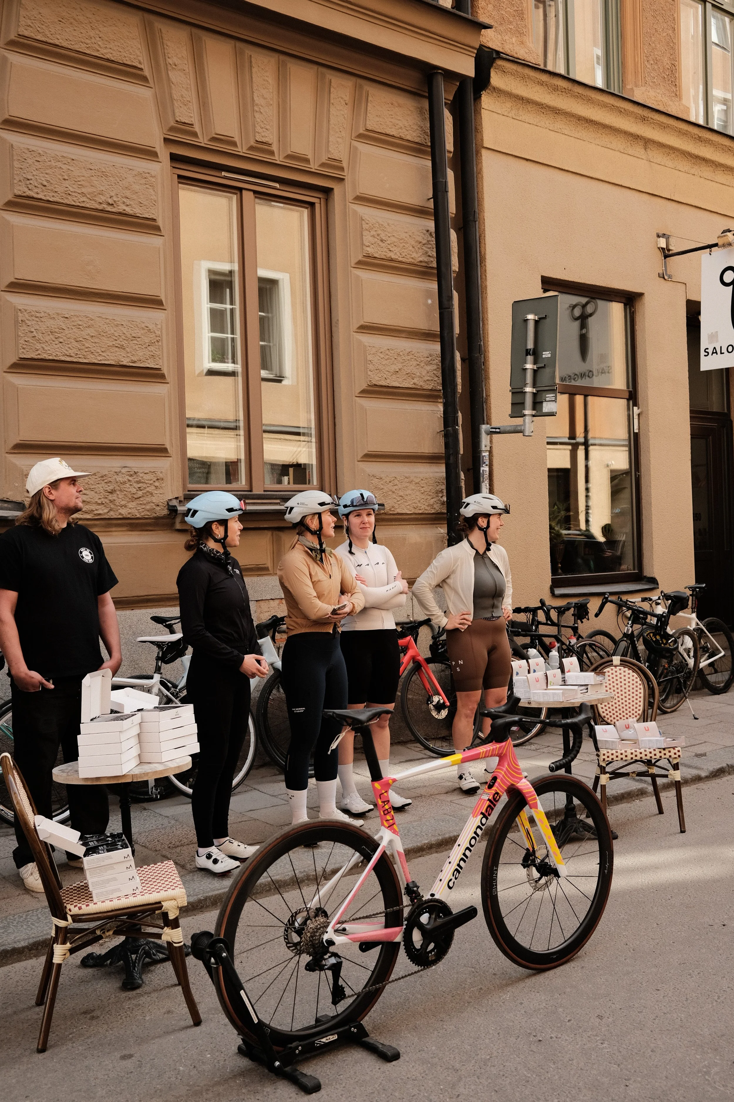 A group of women wearing cycling helmets standing in front of a building, with bikes parked behind them and a Cannondale bicycle in the foreground.