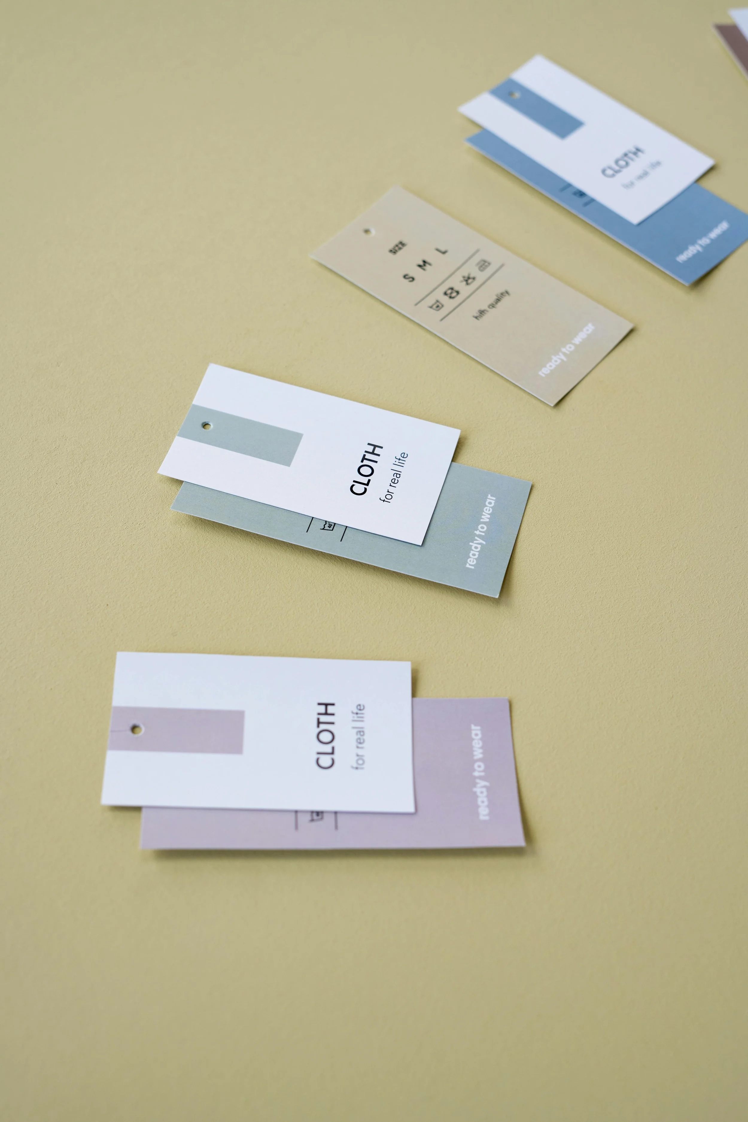 A collection of clothing tags on a yellow surface, each with different colors and text indicating clothing size, material, and readiness for wear.
