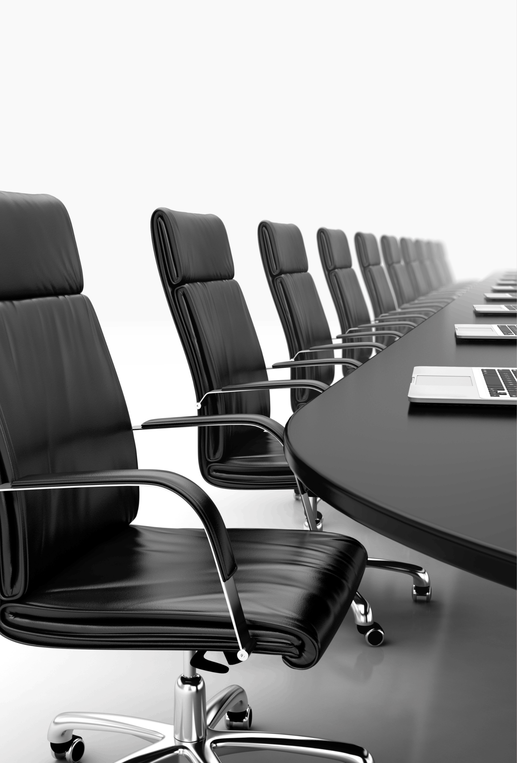 A row of black leather office chairs with chrome armrests and bases, positioned around a long conference table, with laptops and documents on the table.