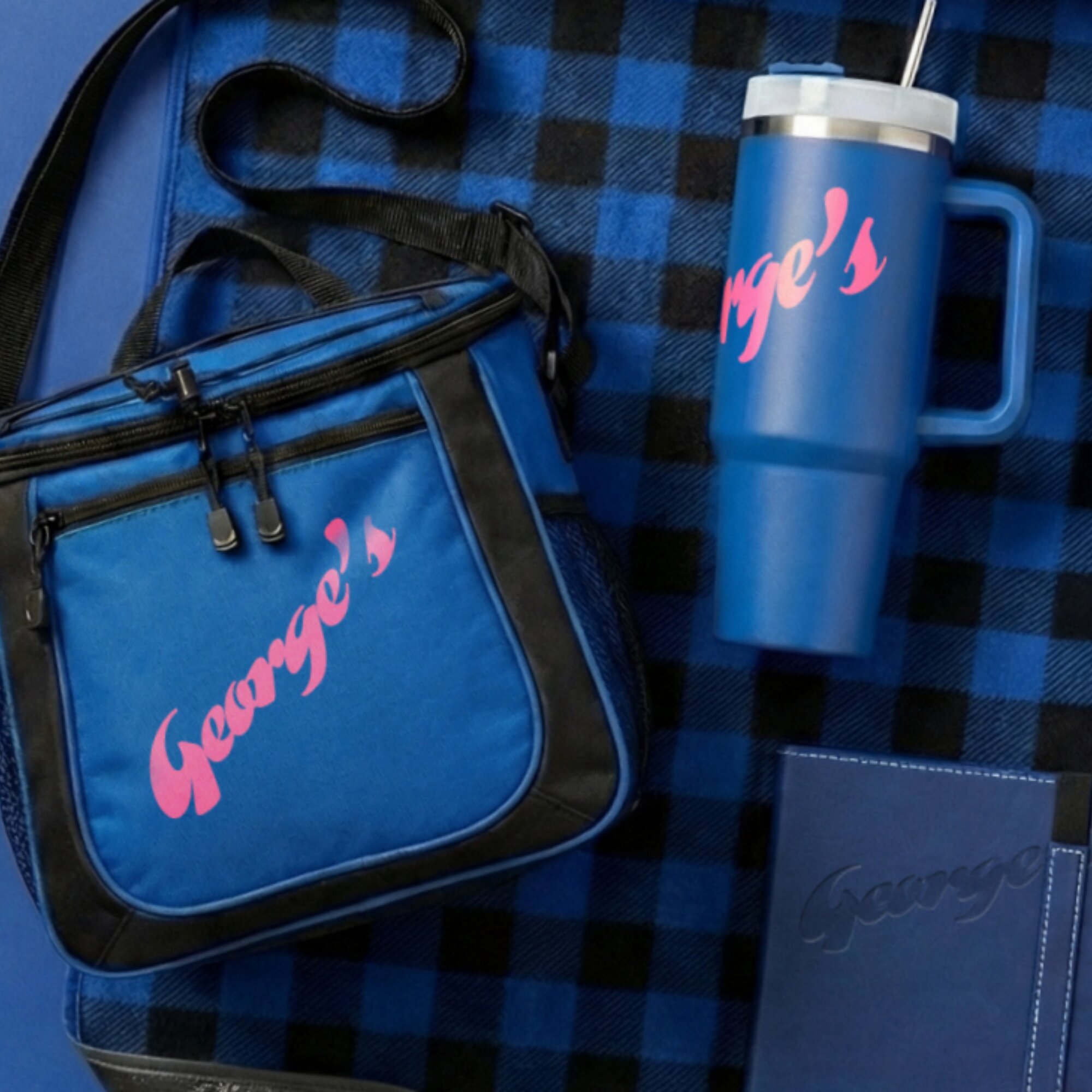 Close-up of a blue thermos with pink lettering reading "Grace's" on a checkered blue and black fabric background, along with a matching blue bag with black zippers and straps.