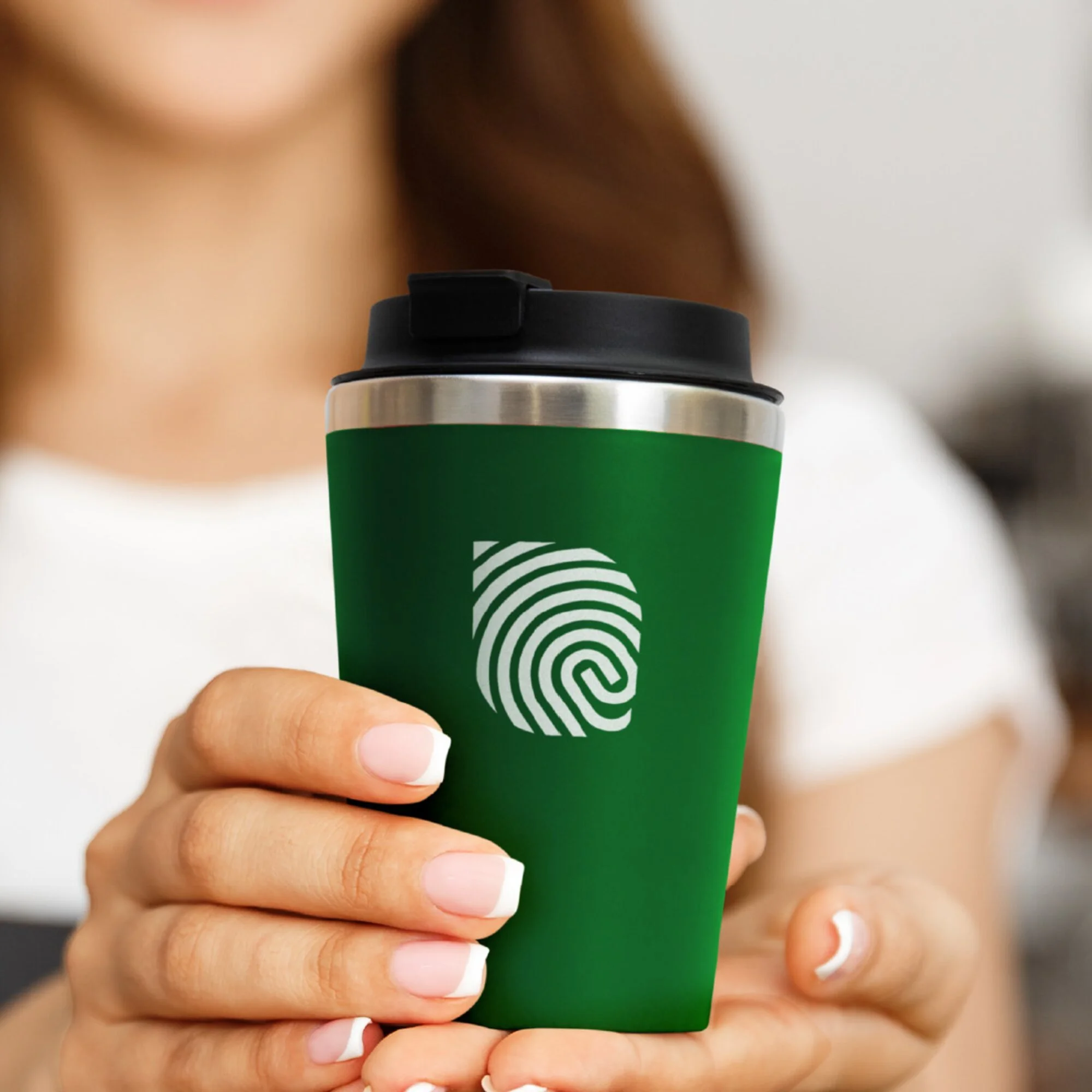 Close-up of a person's hand holding a green disposable coffee cup with a black lid, with a blurred background.
