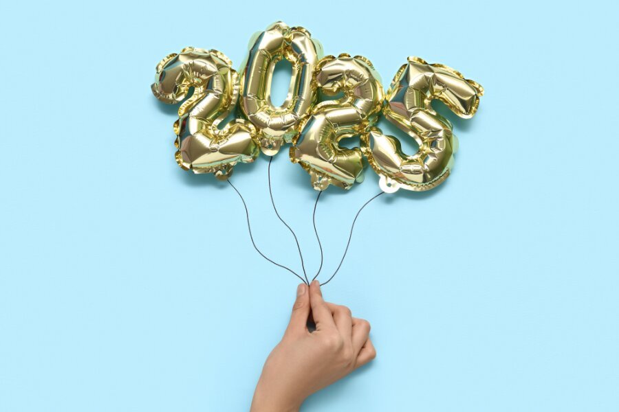 Hand holding four gold balloons shaped as the numbers 2, 0, 2, 5 against a light blue background.