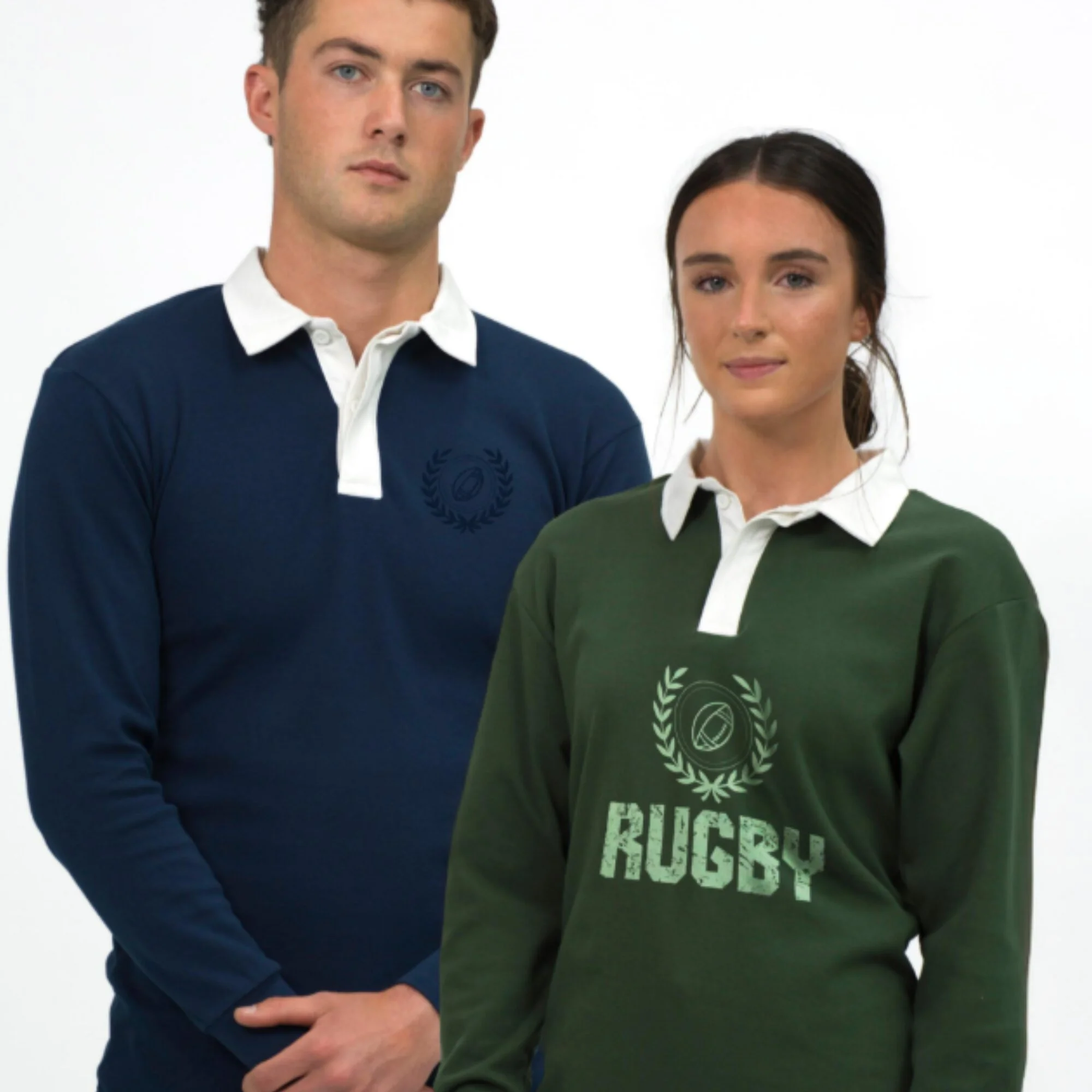 Close-up of two young adults, a man and a woman, standing side by side against a plain white background. The man is wearing a dark blue and white collared shirt, and the woman is wearing a dark green sweatshirt with white text and graphics.