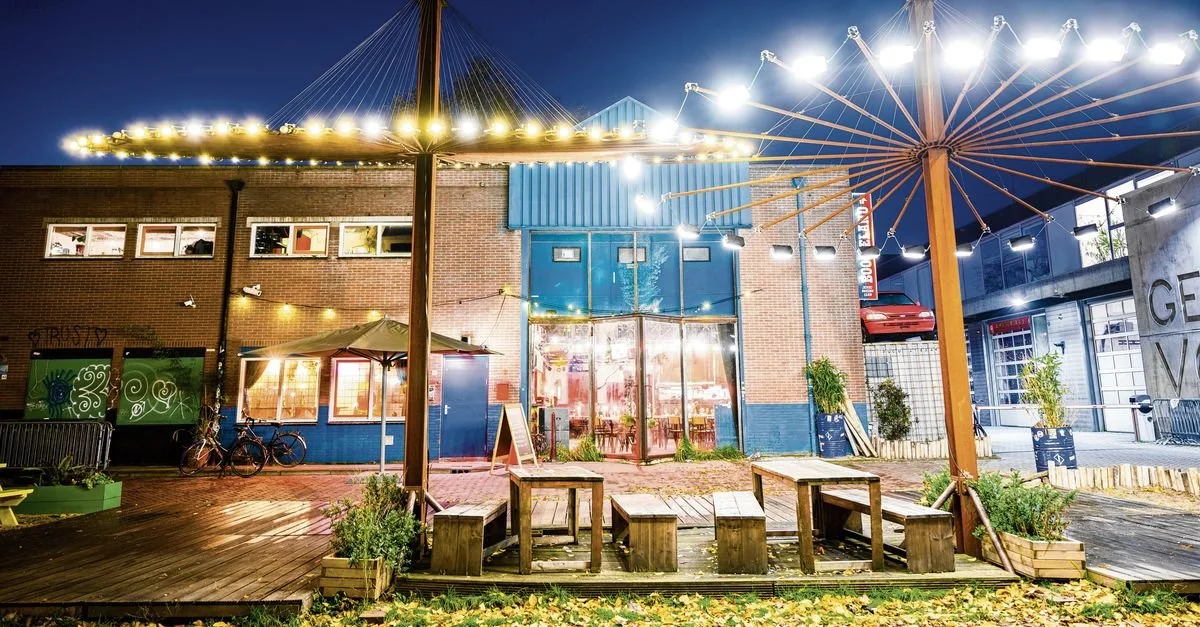 Outdoor urban space at night with string lights, benches, and a brick building with large windows.