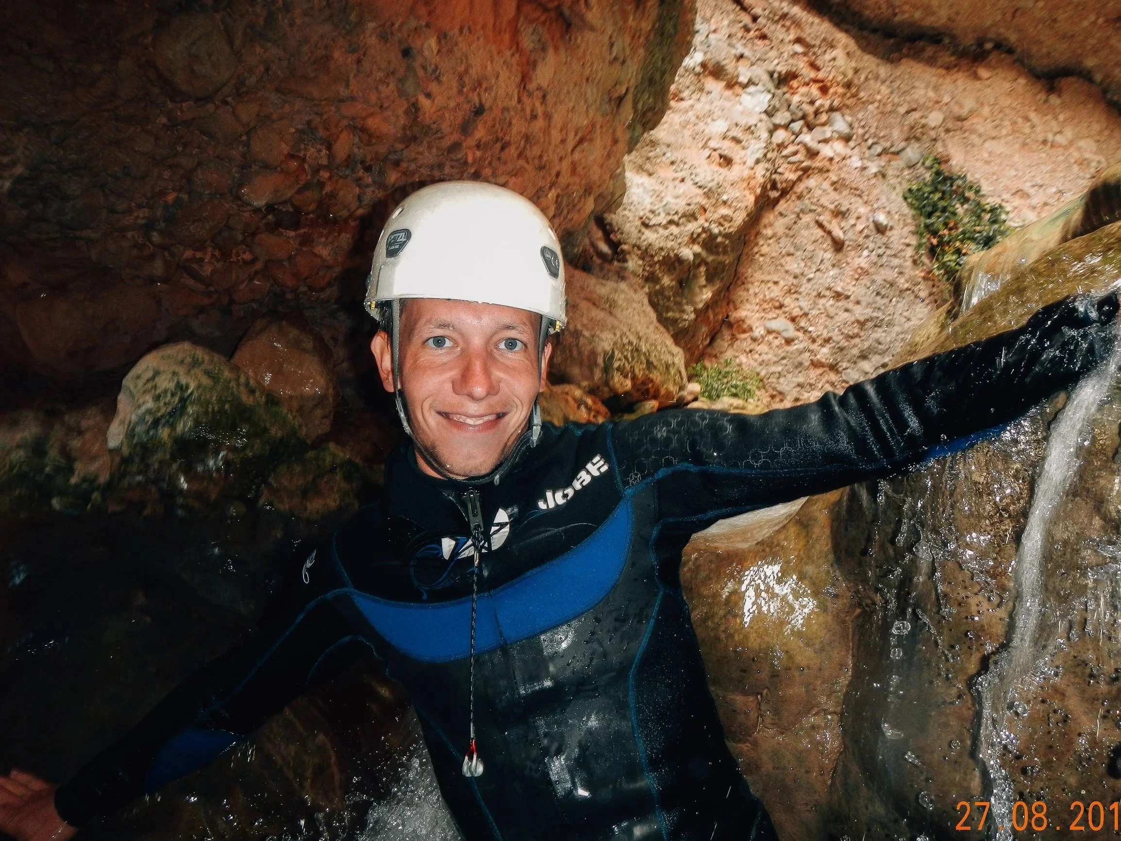 A man with a Petzl helmet, in the canyon, wearing a Jobe wetsuit. With splashing water.
