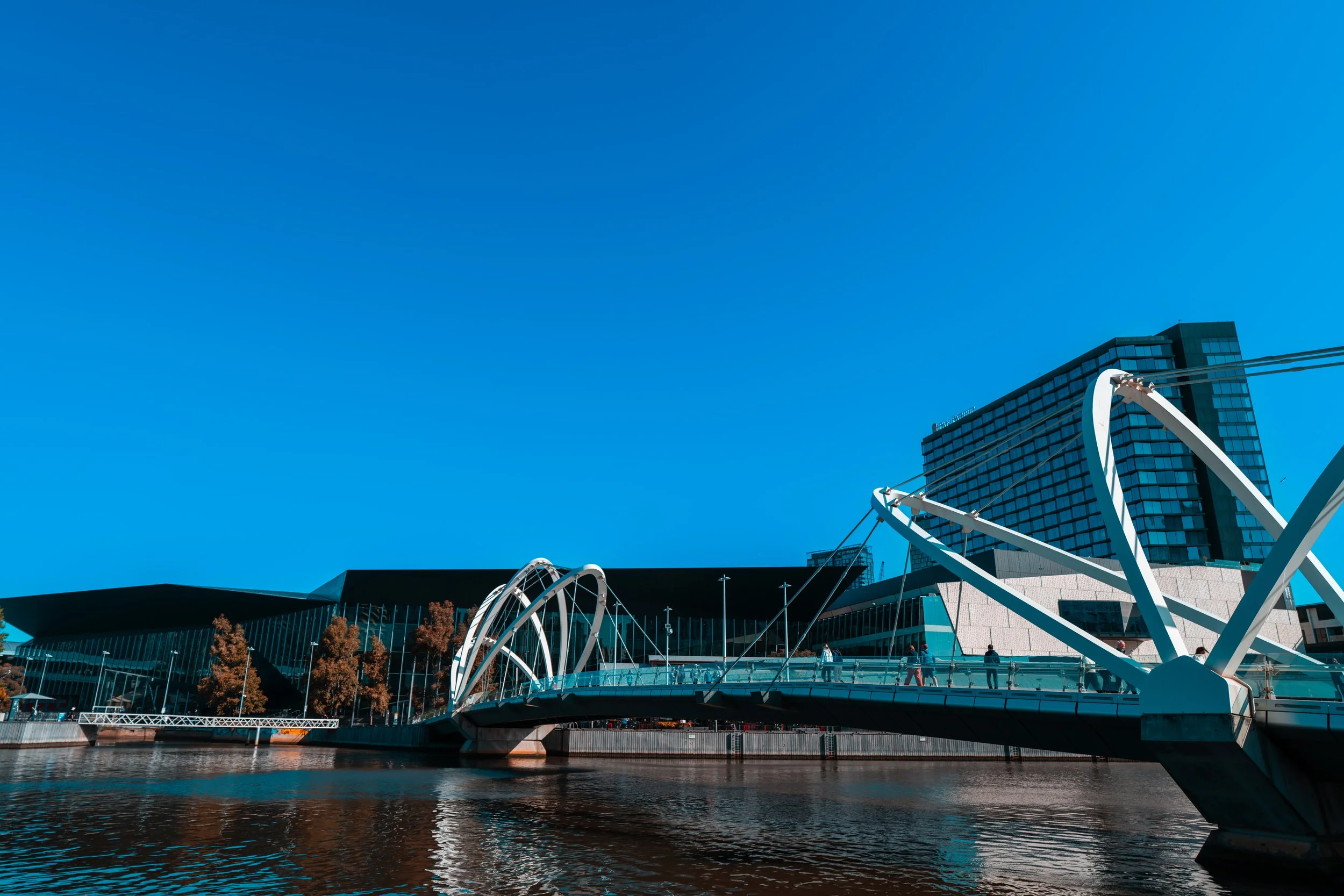 Modern bridge over water with a cityscape in the background, under a clear blue sky.