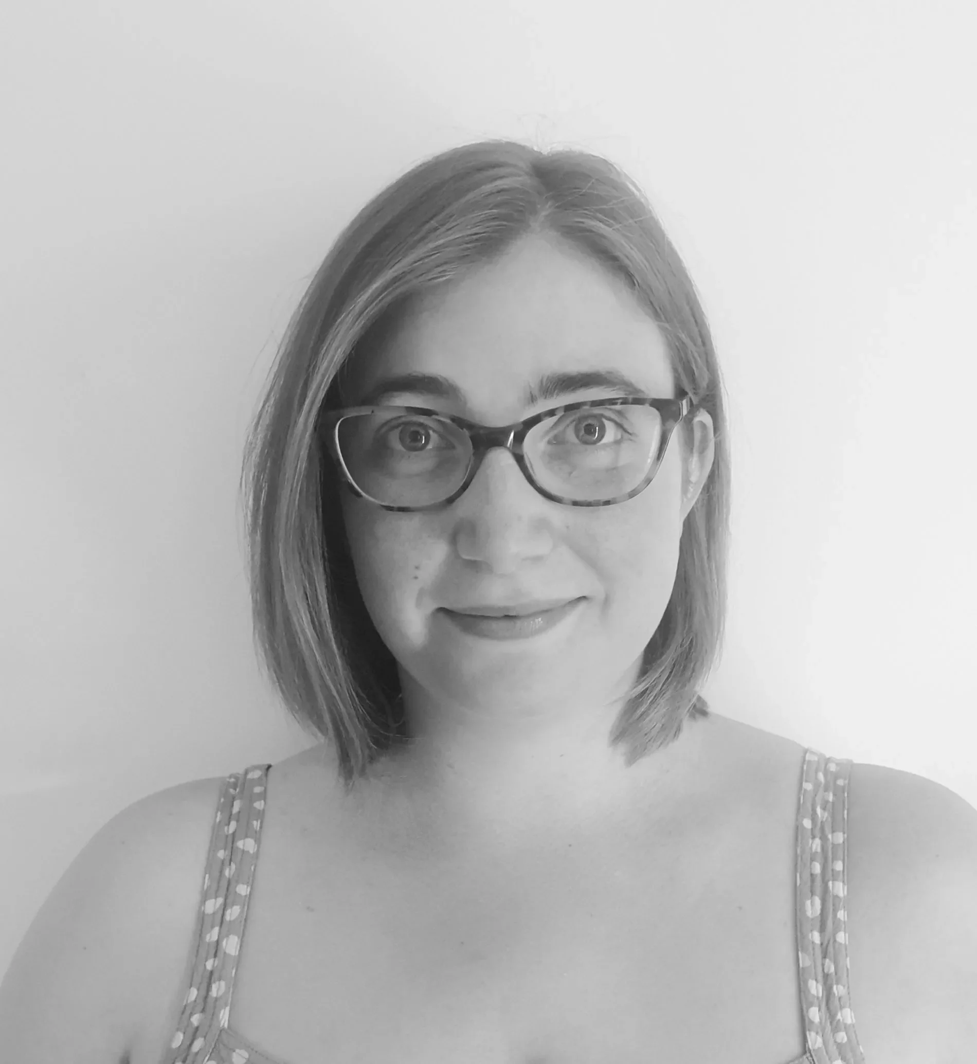 Black and white close-up image of a woman's face, focusing on her eyes and glasses, with shoulder-length hair and wearing a shirt with a striped pattern.
