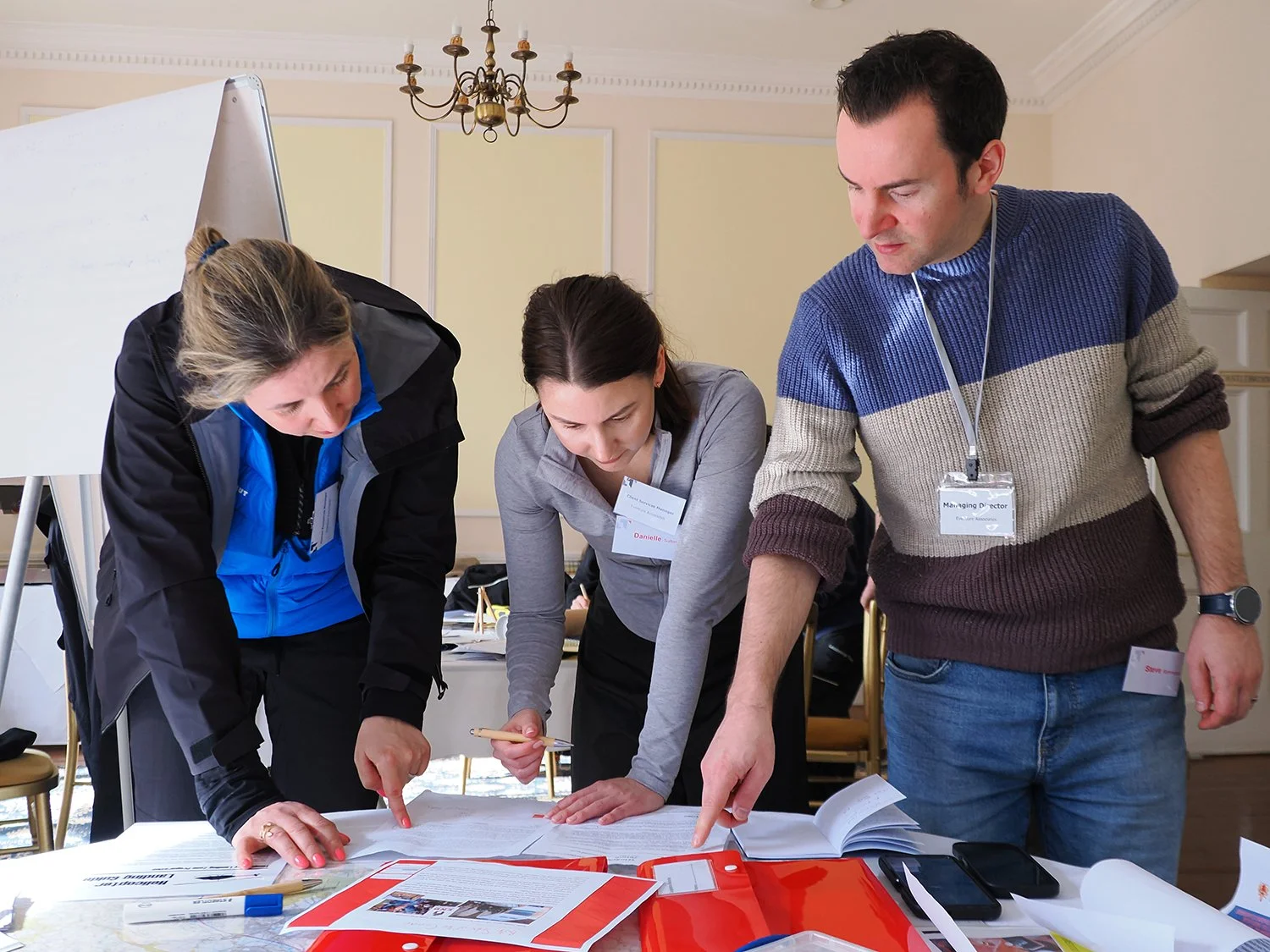 Three people examining documents on a table during a meeting in a conference room.