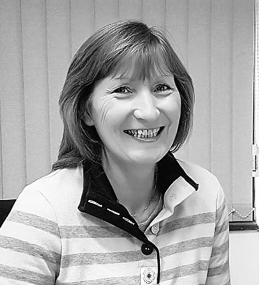 A woman with shoulder-length hair smiling in a black and white photo, wearing a striped polo shirt.