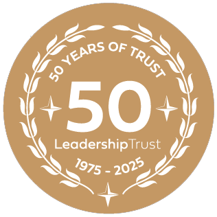 A circular emblem celebrating 50 years of leadership trust from 1975 to 2025, with a gold background, white text, and decorative laurel wreath design.
