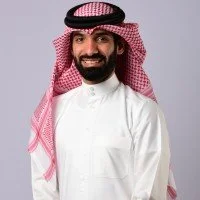 Man wearing traditional Middle Eastern attire with a red and white shemagh and white thobe, smiling.