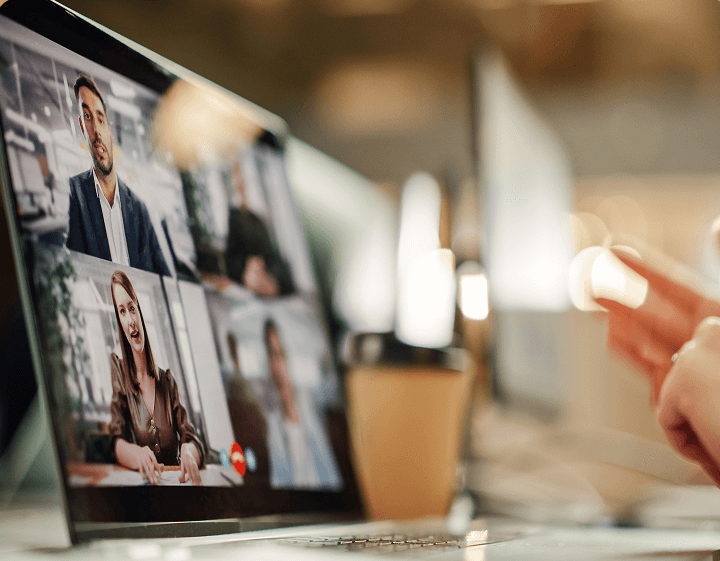 Close-up of a computer screen showing a video conference with multiple participants, including a man in a suit and a woman in a brown jacket.