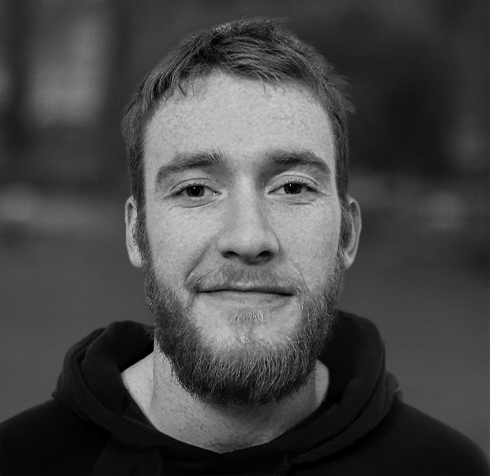 Black and white photo of a young man with a beard and short hair, smiling slightly, wearing a hoodie.
