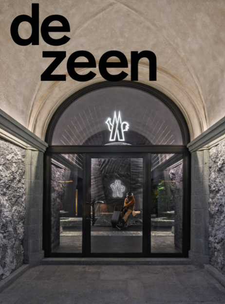 Entrance to a building with the word 'dezeen' in large black letters on the upper left and a neon sign of stylized 'YF' inside, visible through glass doors.