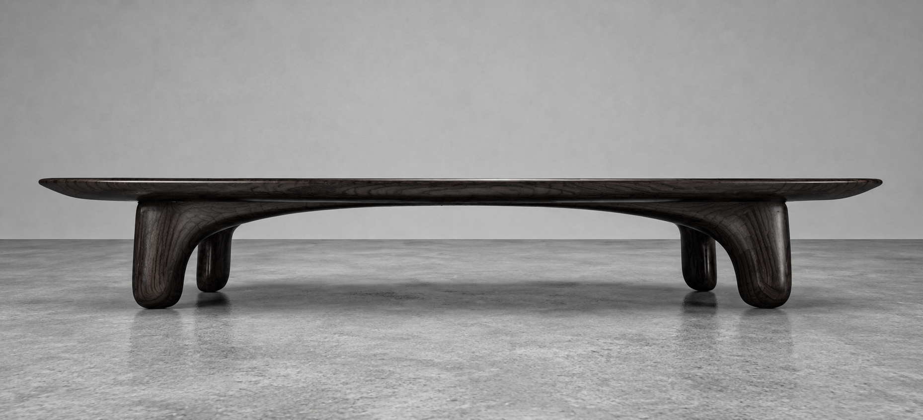 A modern, dark wooden low-profile bench with curved legs, set against a plain gray wall and concrete floor.