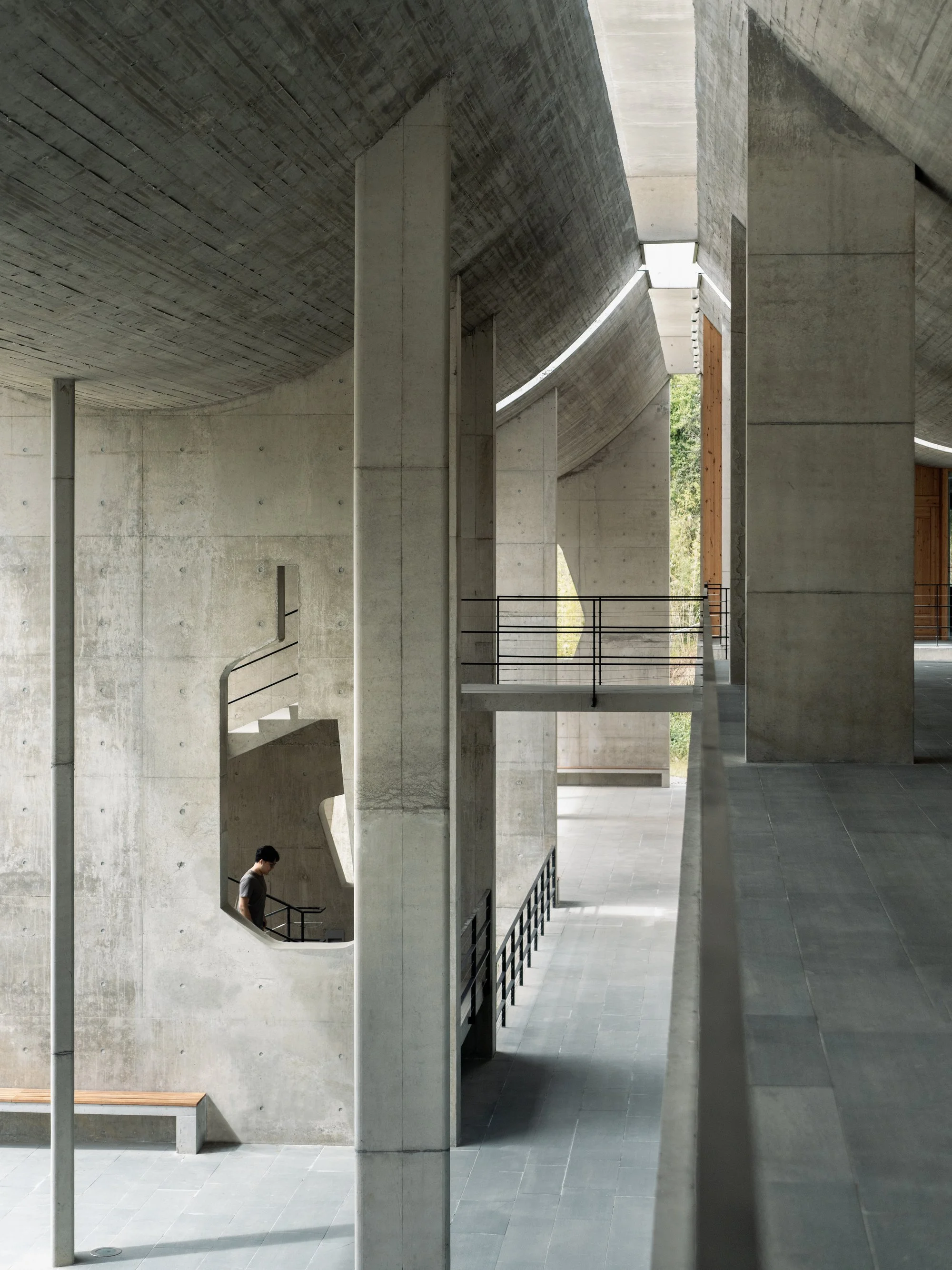 Modern architectural interior featuring concrete walls, a staircase, and large openings with natural light.