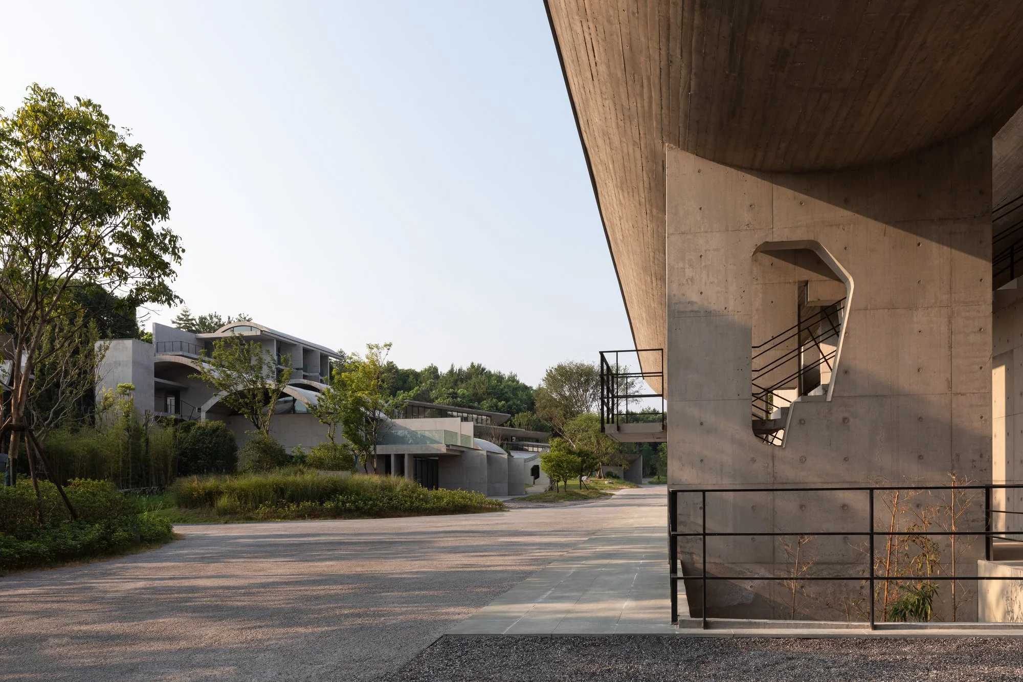 Modern concrete and wood residential buildings with outdoor stairs, trees, and a pathway, during daytime.