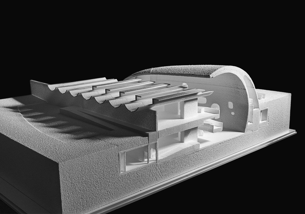 A black and white architectural model of a building with curved and angular elements, resting on a textured base.