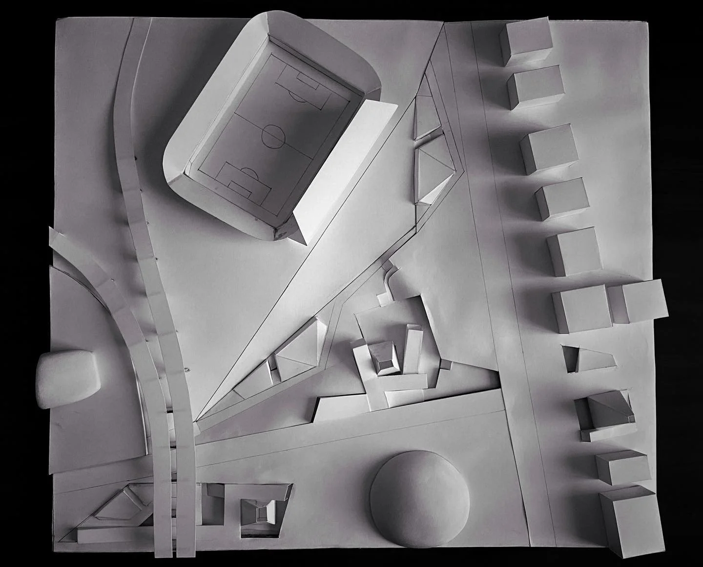 A white paper architectural model of a sports complex, including a football field, small buildings, and pathways.