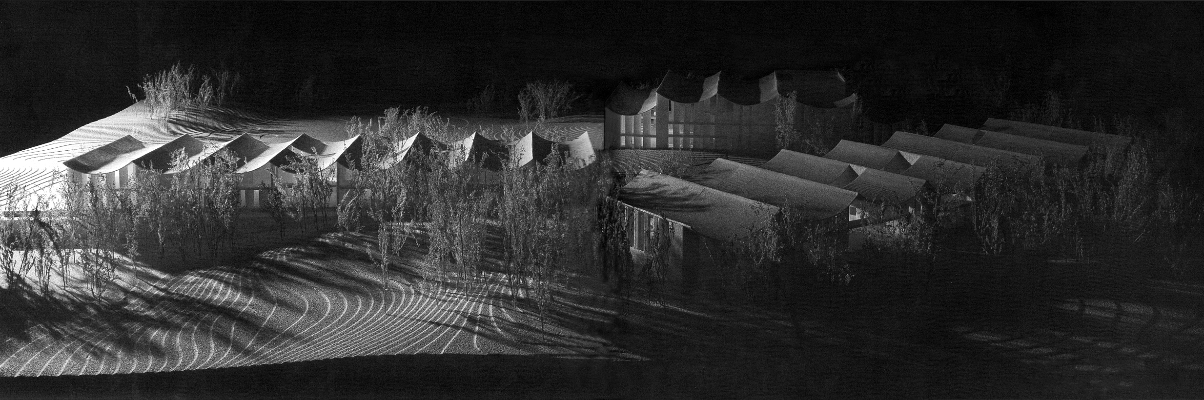 Nighttime aerial view of a modern building with curved roofs, surrounded by trees and illuminated by outdoor lighting, with shadows cast on the ground.