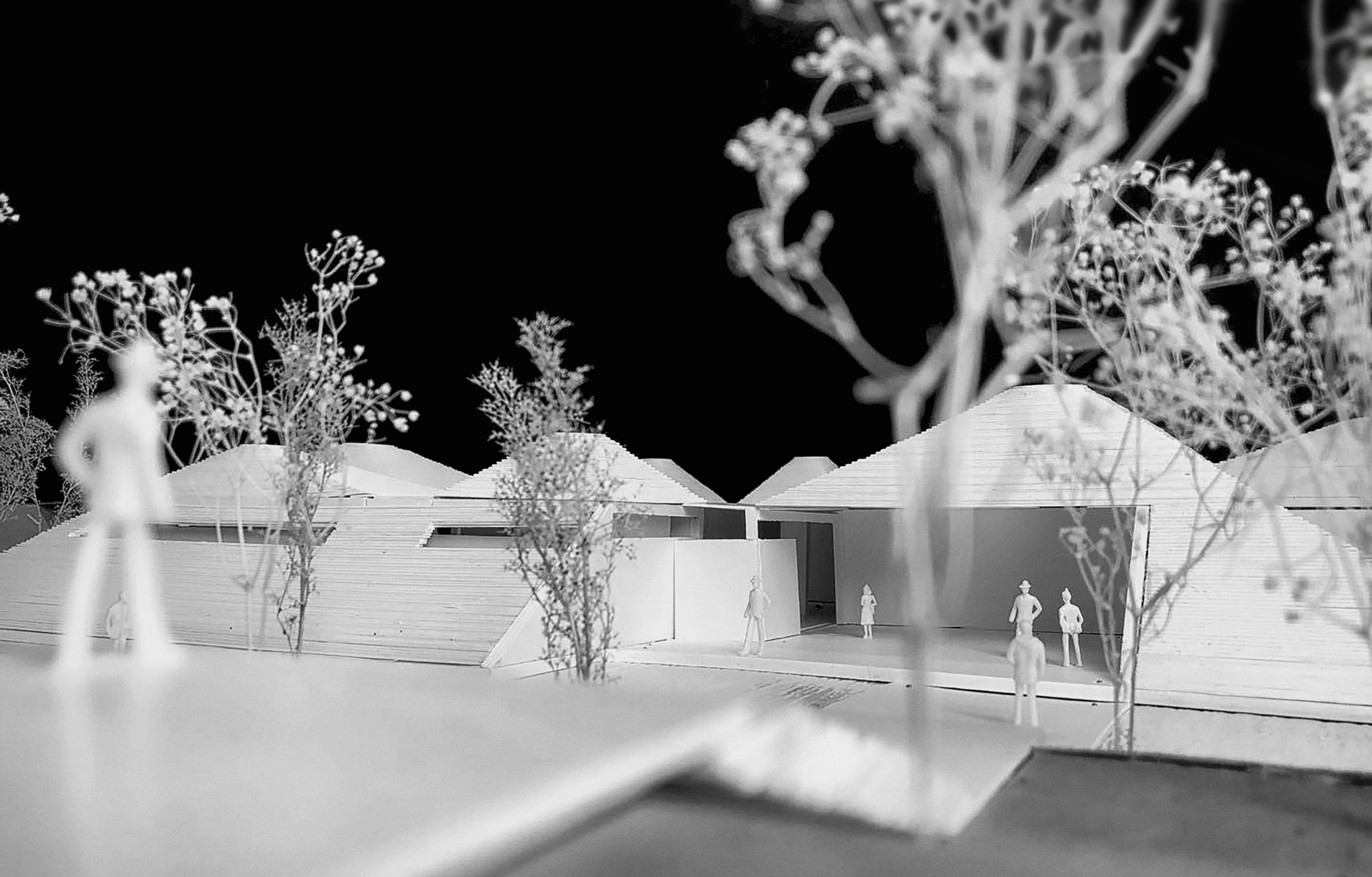 Black and white architectural model of a modern building with figurines and trees in the foreground