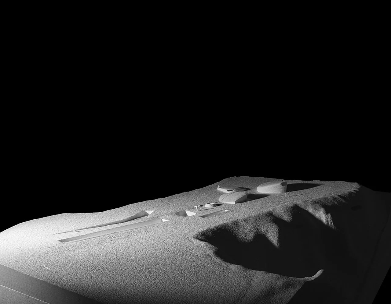 Magnified view of a lunar module model on a textured white surface with shadows and contours, against a black background.