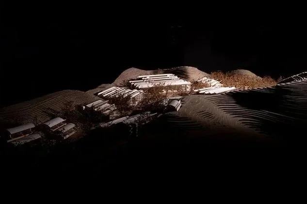 Model of a landscape with rolling hills and multiple buildings, illuminated against a dark background.