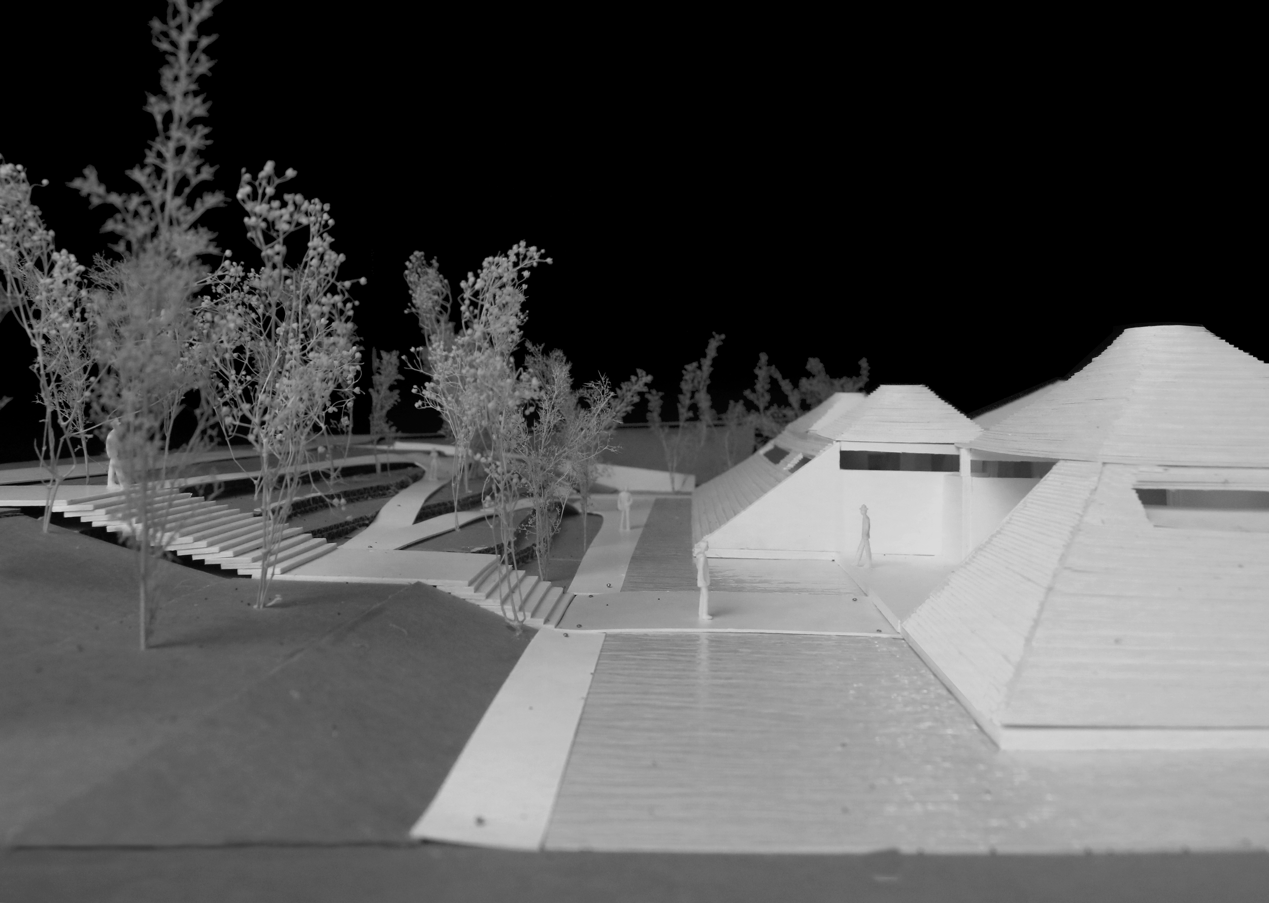 Architectural model of a modern building complex with surrounding trees, pathways, and stairs, set against a dark background.